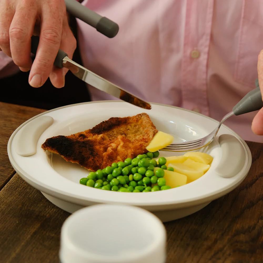 Teller mit Essen: Fisch, Erbsen, Kartoffeln. Person schneidet Fisch mit Messer.