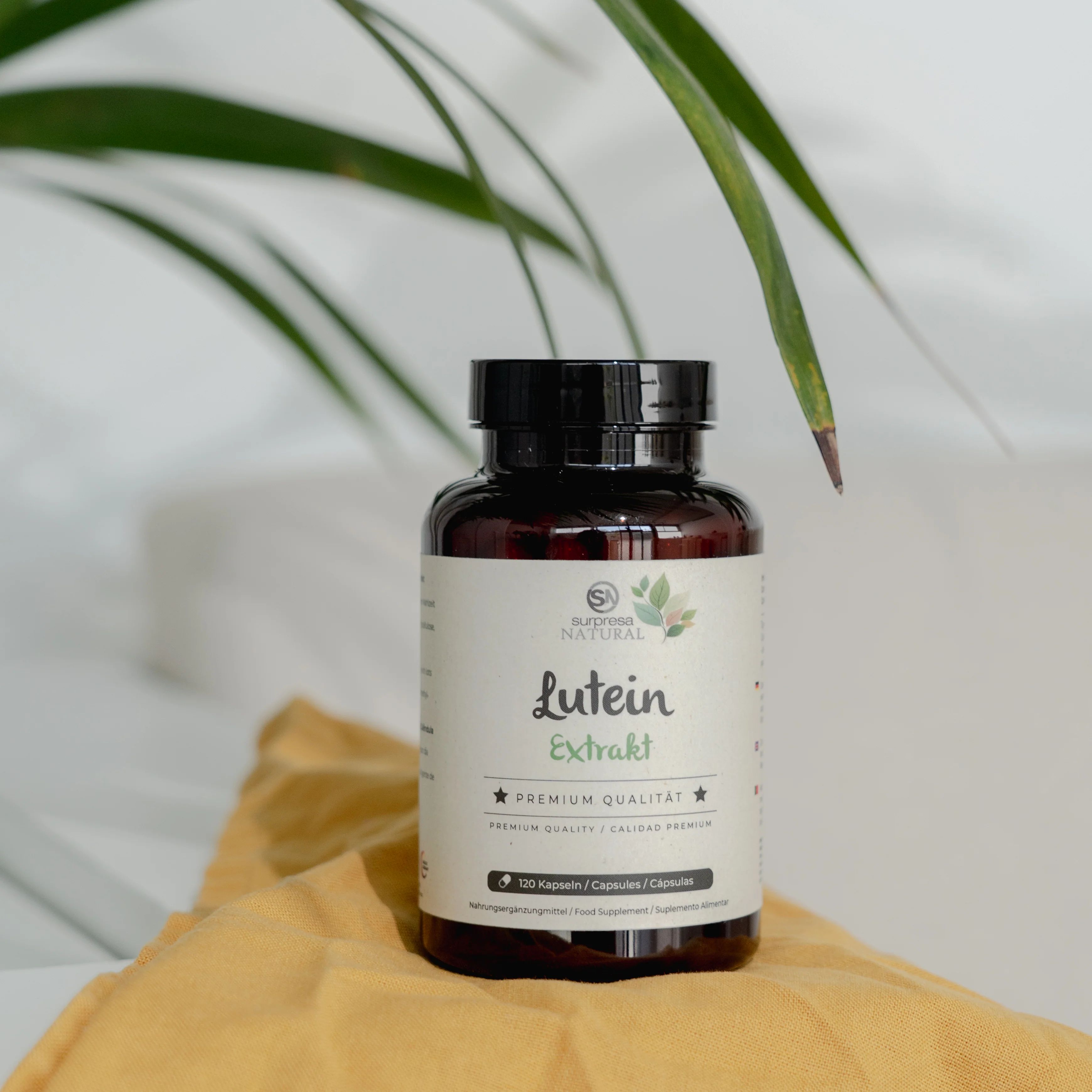 Braune Flasche mit Etikett. Aufschrift: Lutein Extrakt, Premium Qualität. 120 Kapseln. Marke: Surpresa Natural. Auf gelbem Tuch.