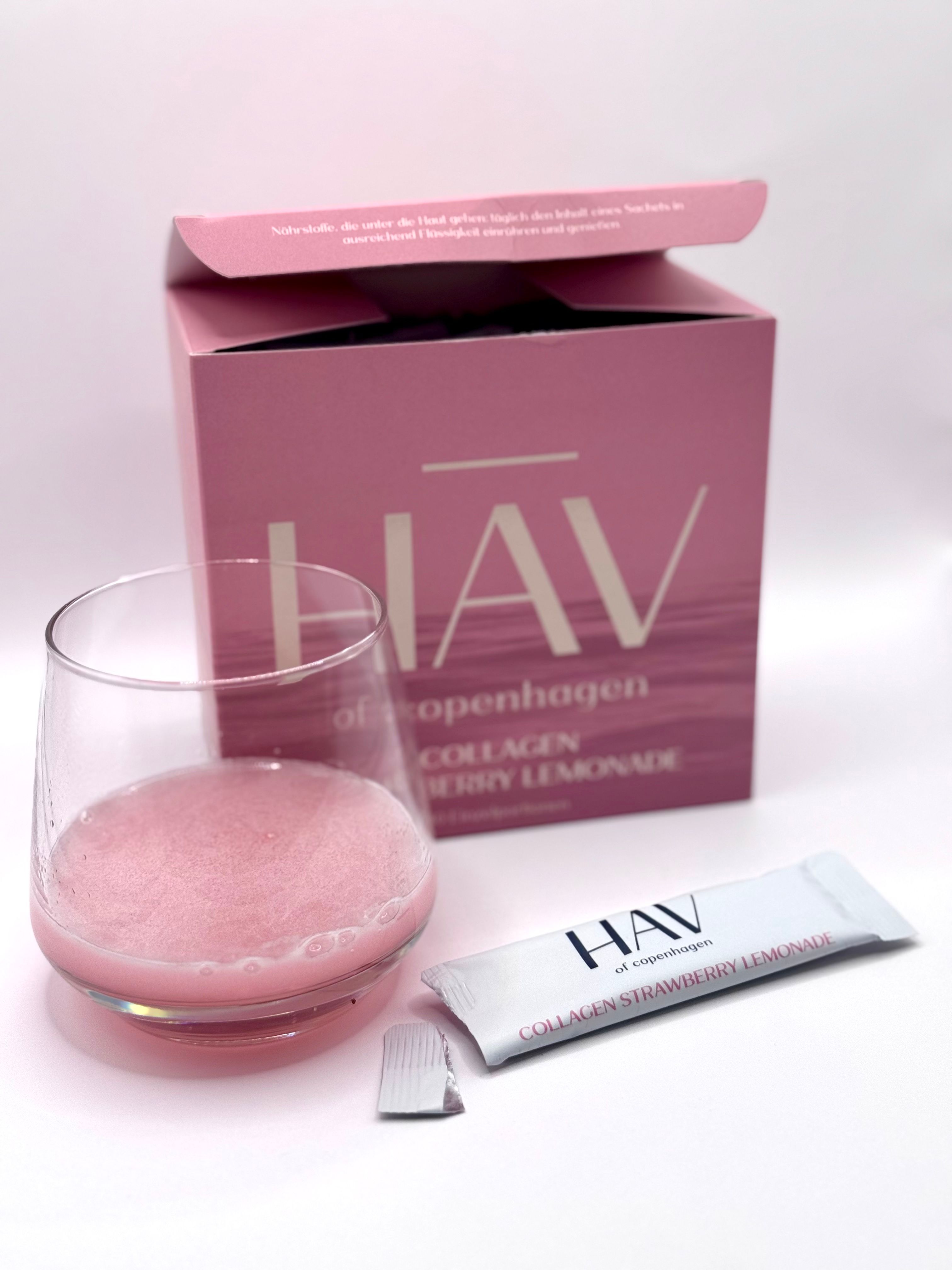 Glas mit rosa Flüssigkeit, Beutel und offene Verpackung. HAV Collagen Strawberry Lemonade.