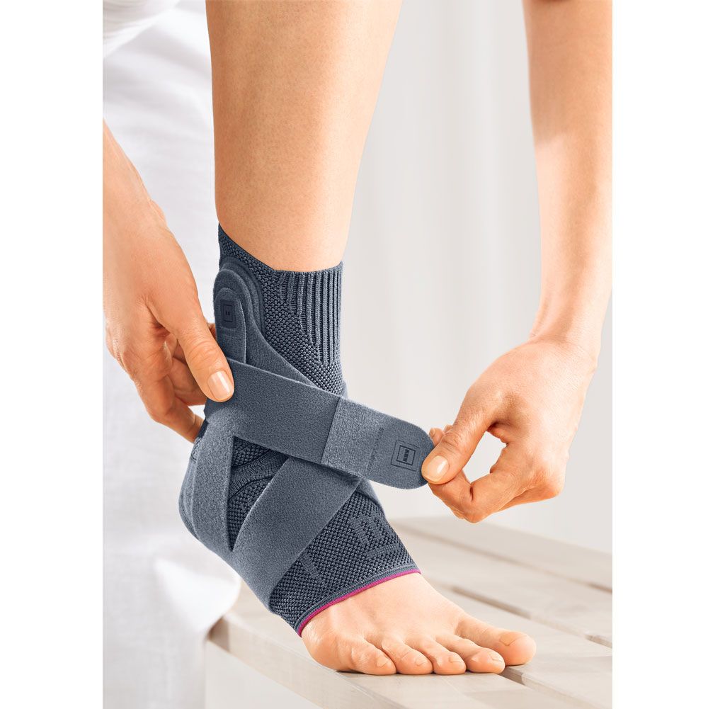 Graue Sprunggelenkbandage. Hände befestigen Gurte. Roter Akzent am Saum. Produkt am Fuß. Auf hellem Hintergrund.