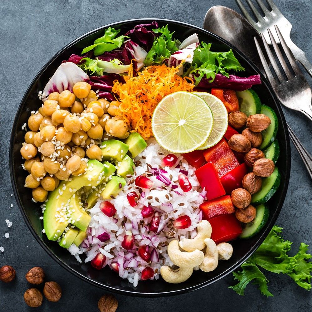 Schwarze Schüssel mit Bowl. Enthält Kichererbsen, Avocado, Reis, Granatapfel, Gemüse, Nüsse und Limettenscheiben.