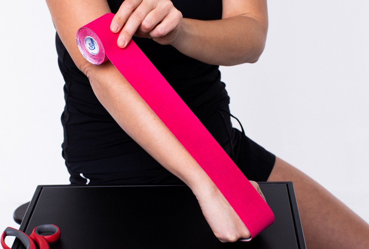 Person rollt pinkfarbenes Tape auf dem Arm ab. Eine Schere liegt daneben.