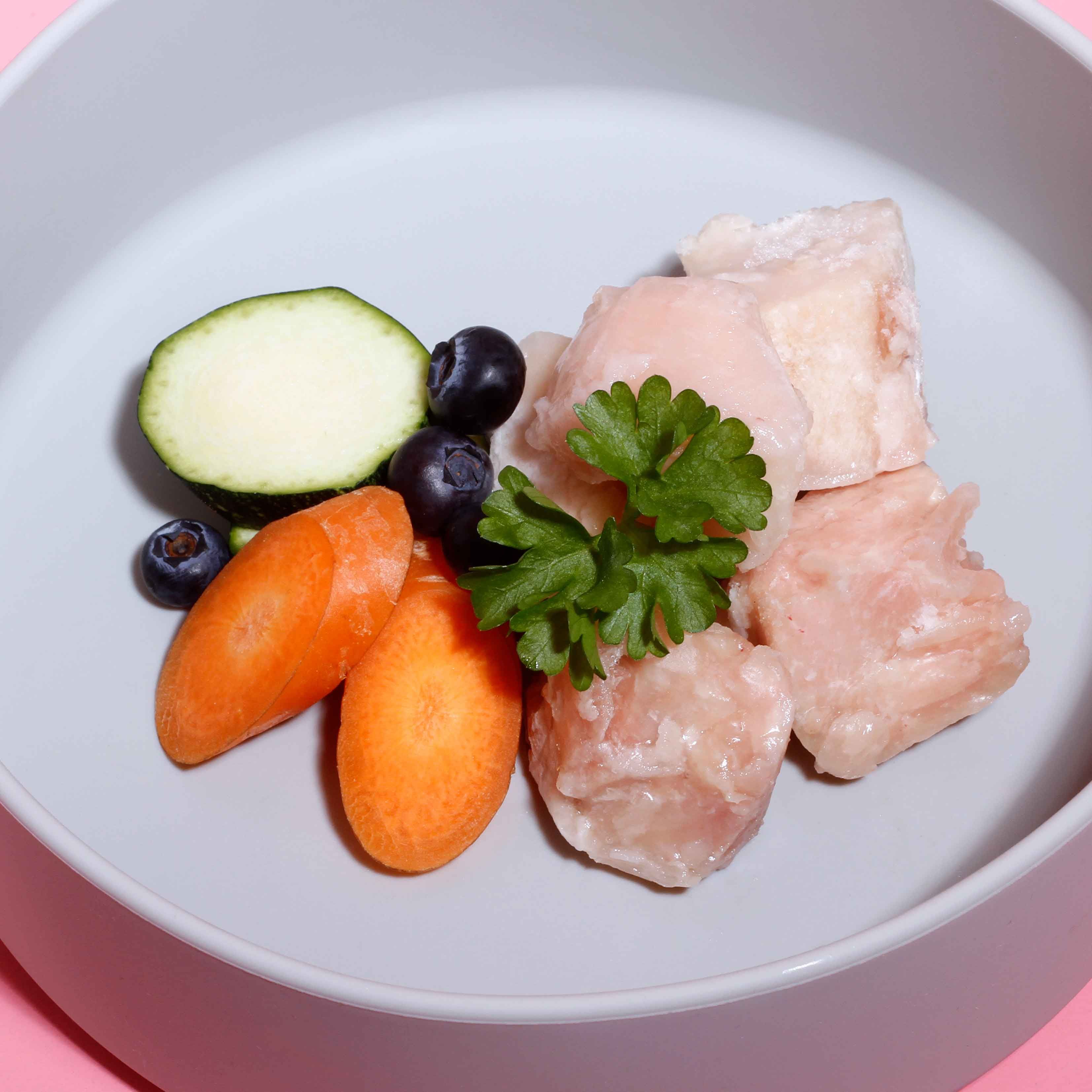 Hundefutter mit Gemüse und Fleisch in einer Schüssel. Enthalten sind Karotten, Zucchini, Blaubeeren und Fleischstücke.