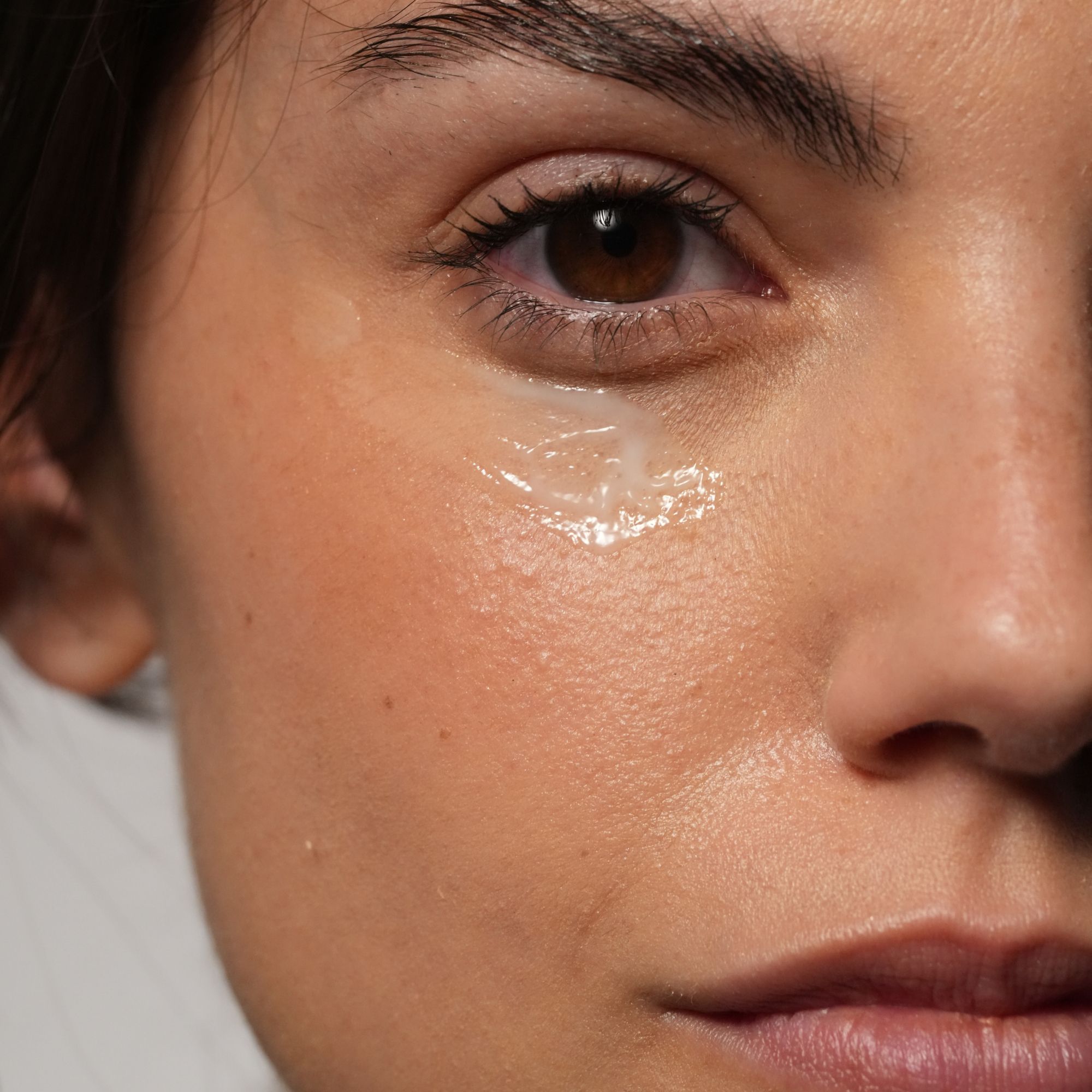 Nahaufnahme eines Auges mit aufgetragener, transparenter Augencreme.