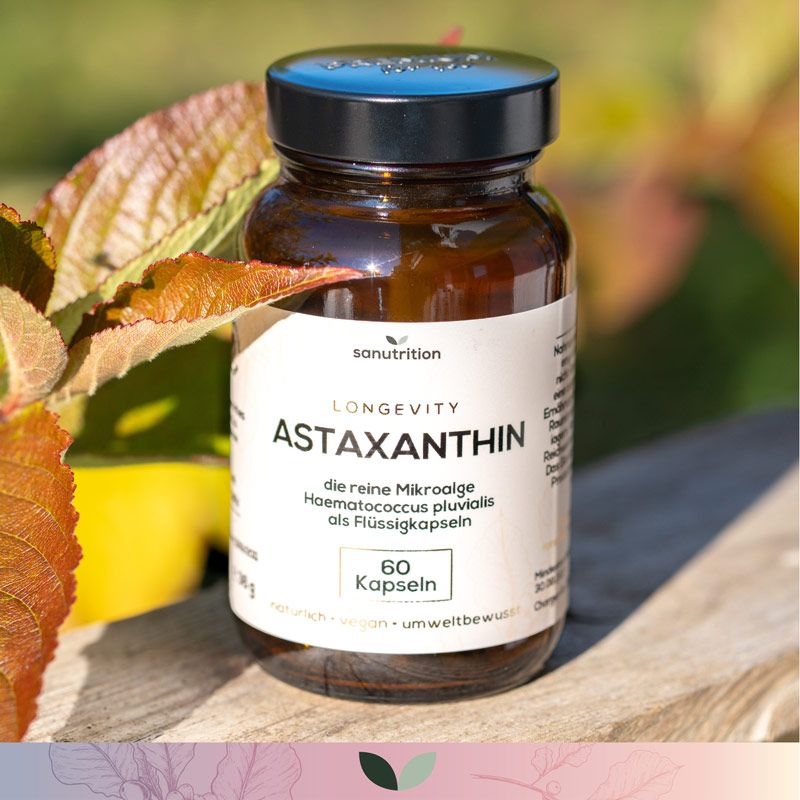 Braune Glasflasche mit schwarzem Deckel. Etikett mit "Astaxanthin" und "60 Kapseln". Marke: Sanutrition. Im Hintergrund Blätter.