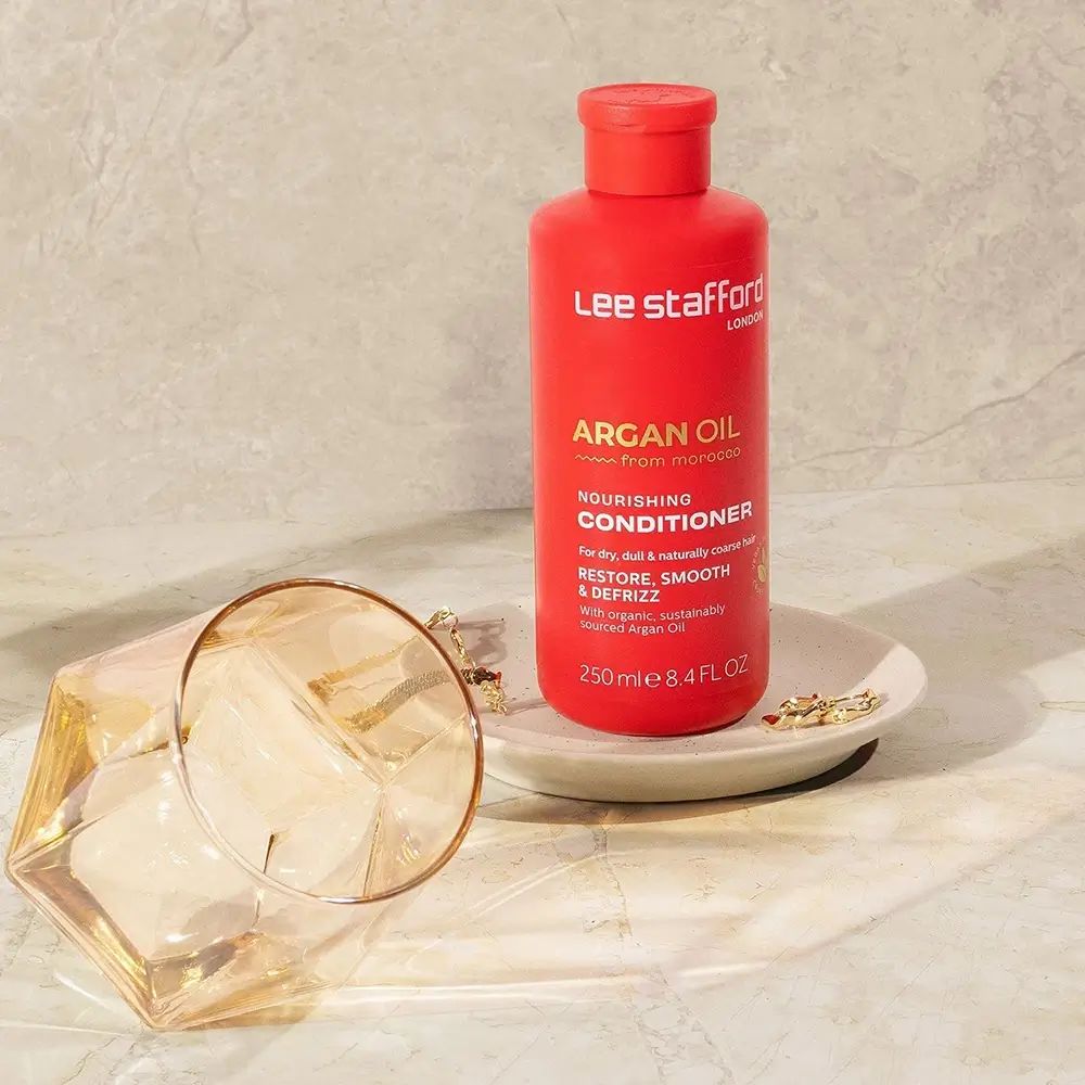 Rote Flasche auf einem Teller. Aufschrift: Argan Oil, Nourishing Conditioner. Glas und Schmuck daneben.