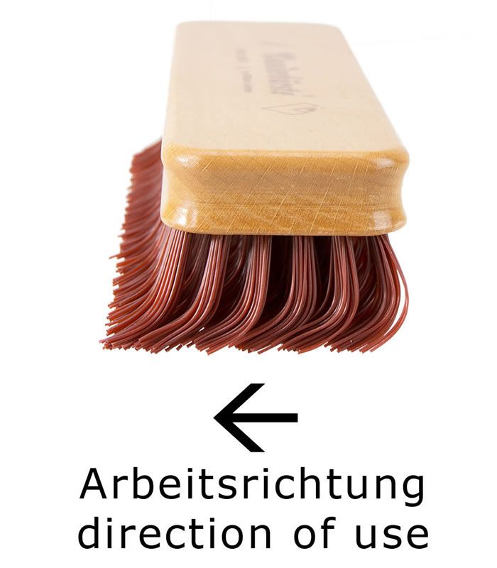 Bürste mit Holzgriff und roten Borsten. Pfeil mit Aufschrift: Arbeitsrichtung/direction of use.