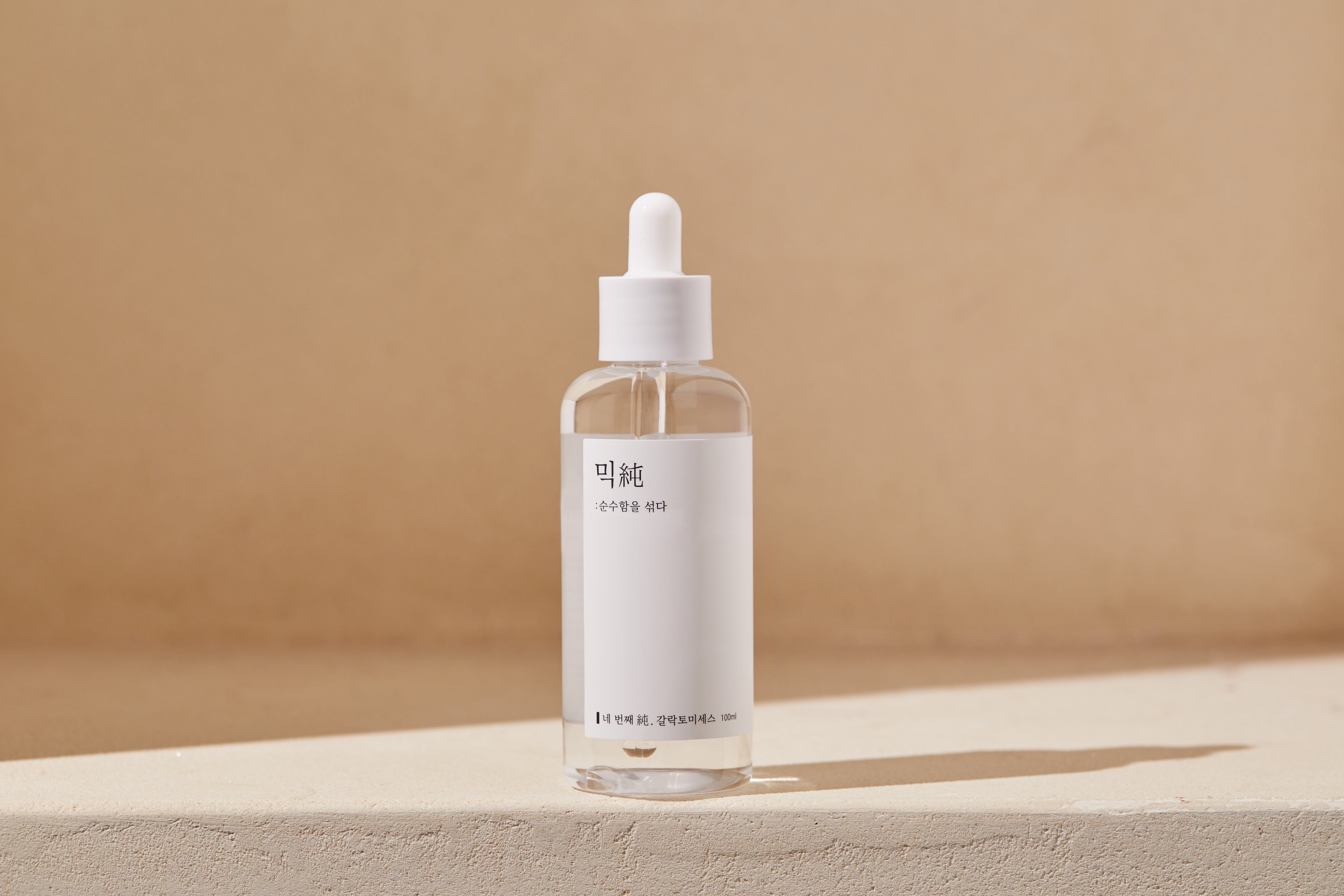 Klare Flasche mit weißem Etikett und Pipette. Auf einer Oberfläche platziert. Hintergrund: Beige.