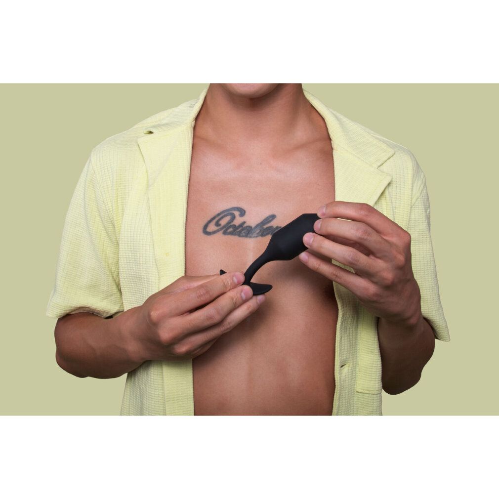 Person hält schwarzen Plug. Brust mit Tattoo. Gelbes Hemd.