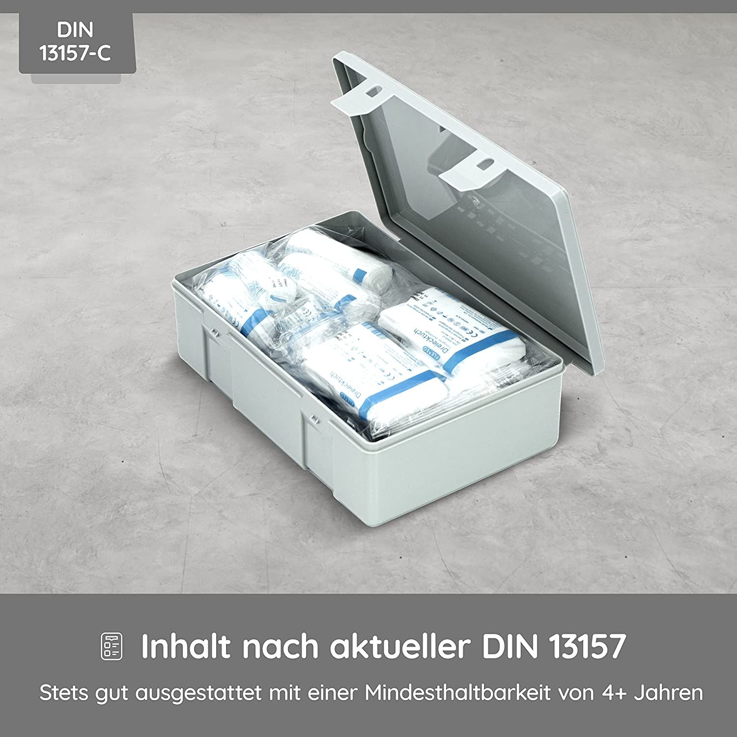 Geöffnete graue Verbandkasten mit Inhalt. DIN 13157-C. Enthält Verbandsmaterial. Deckel teilweise geöffnet.