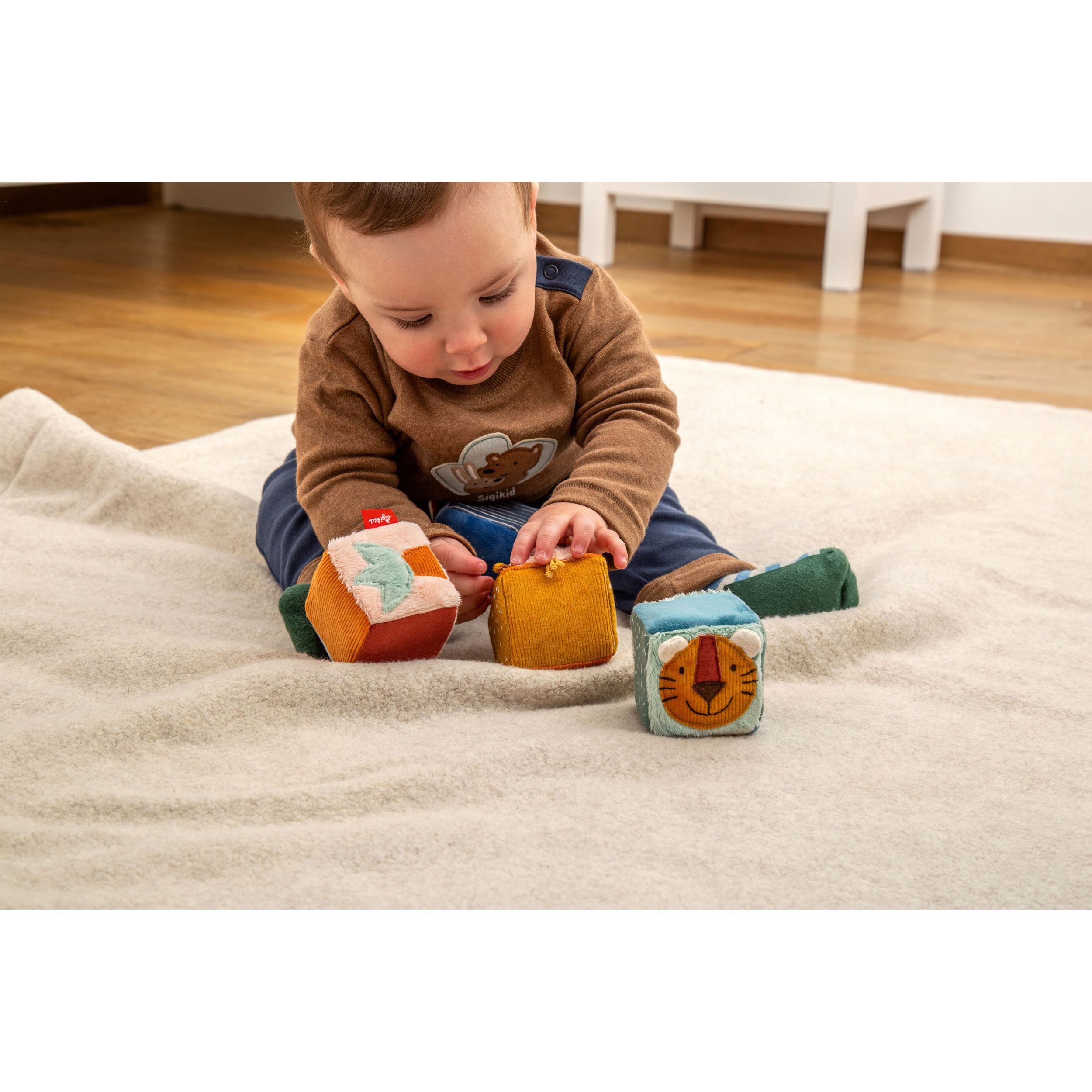 Baby spielt mit drei bunten Stoffwürfeln. SIGIKID-Logo auf einem Würfel sichtbar.