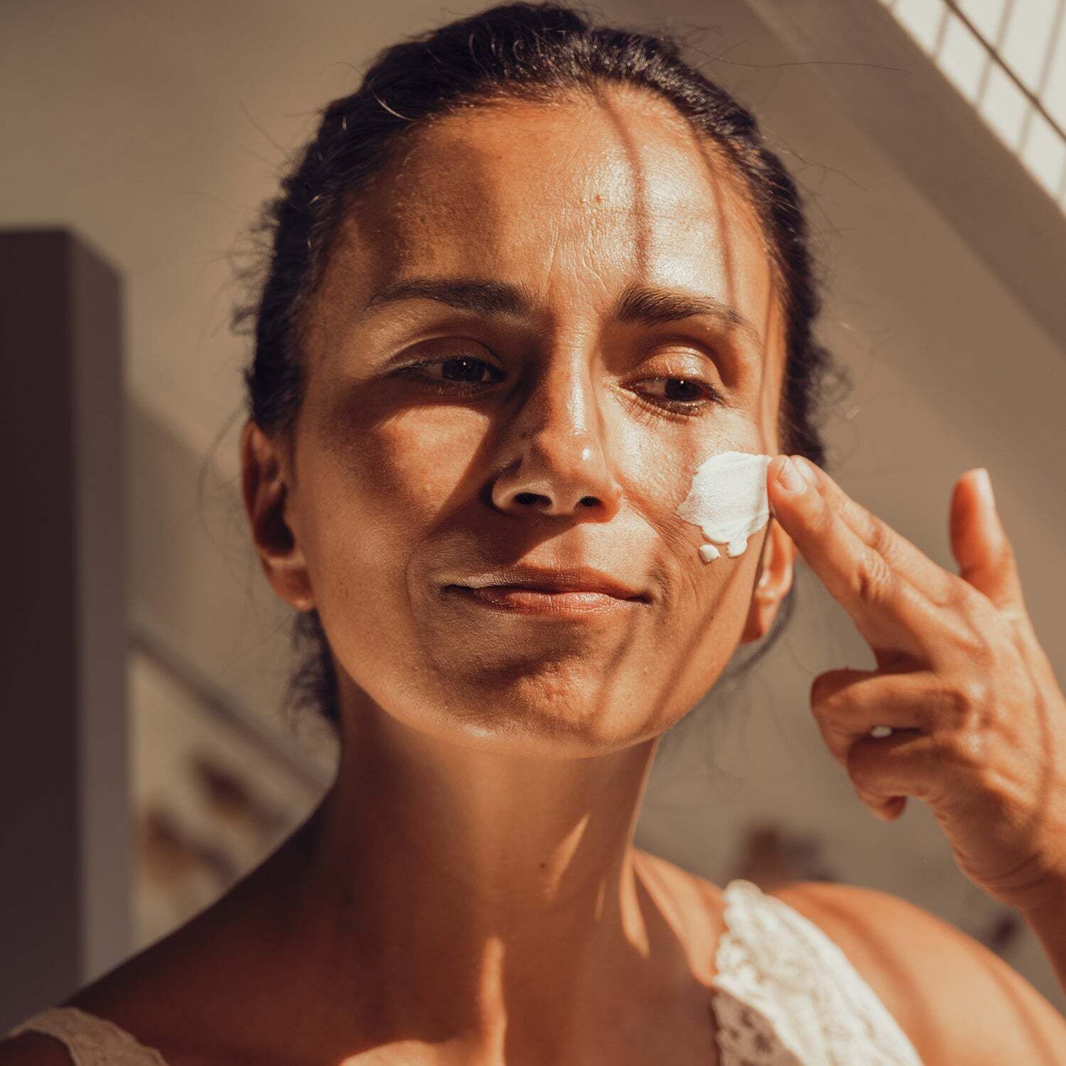 Frau trägt Sonnenfluid auf ihr Gesicht auf. Helle Haut, Sonnenlicht. Weiße Kleidung.