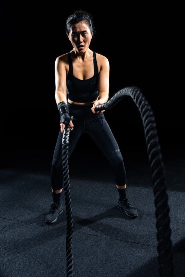 Athletin beim Training mit Seilen. Sie trägt eine schwarze Sportbekleidung und eine Handgelenkbandage.