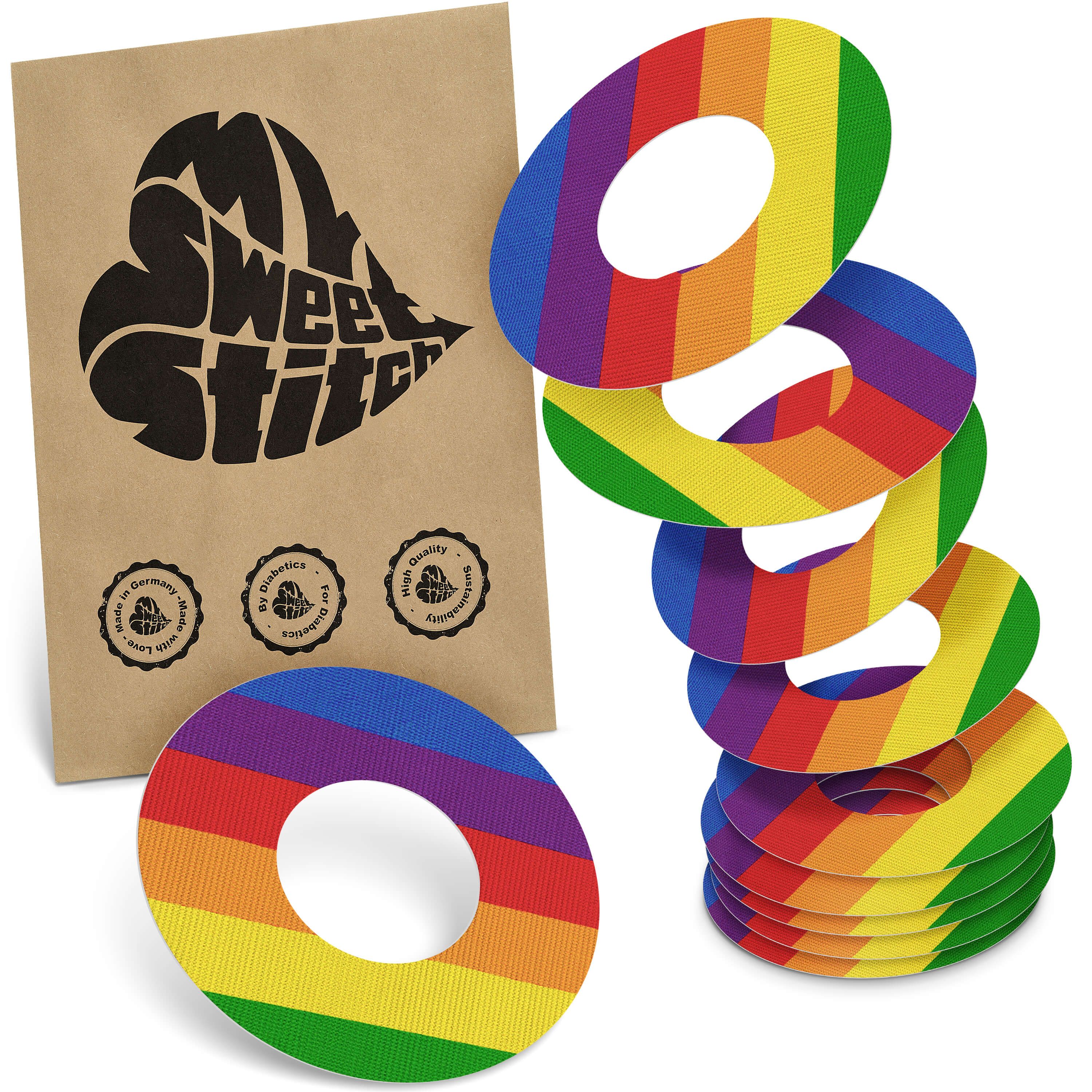 Mehrere Fixierringe mit Regenbogenmuster und eine braune Verpackung mit Logo. Ringe in Regenbogenfarben, kreisförmig. Verpackung mit Logo.