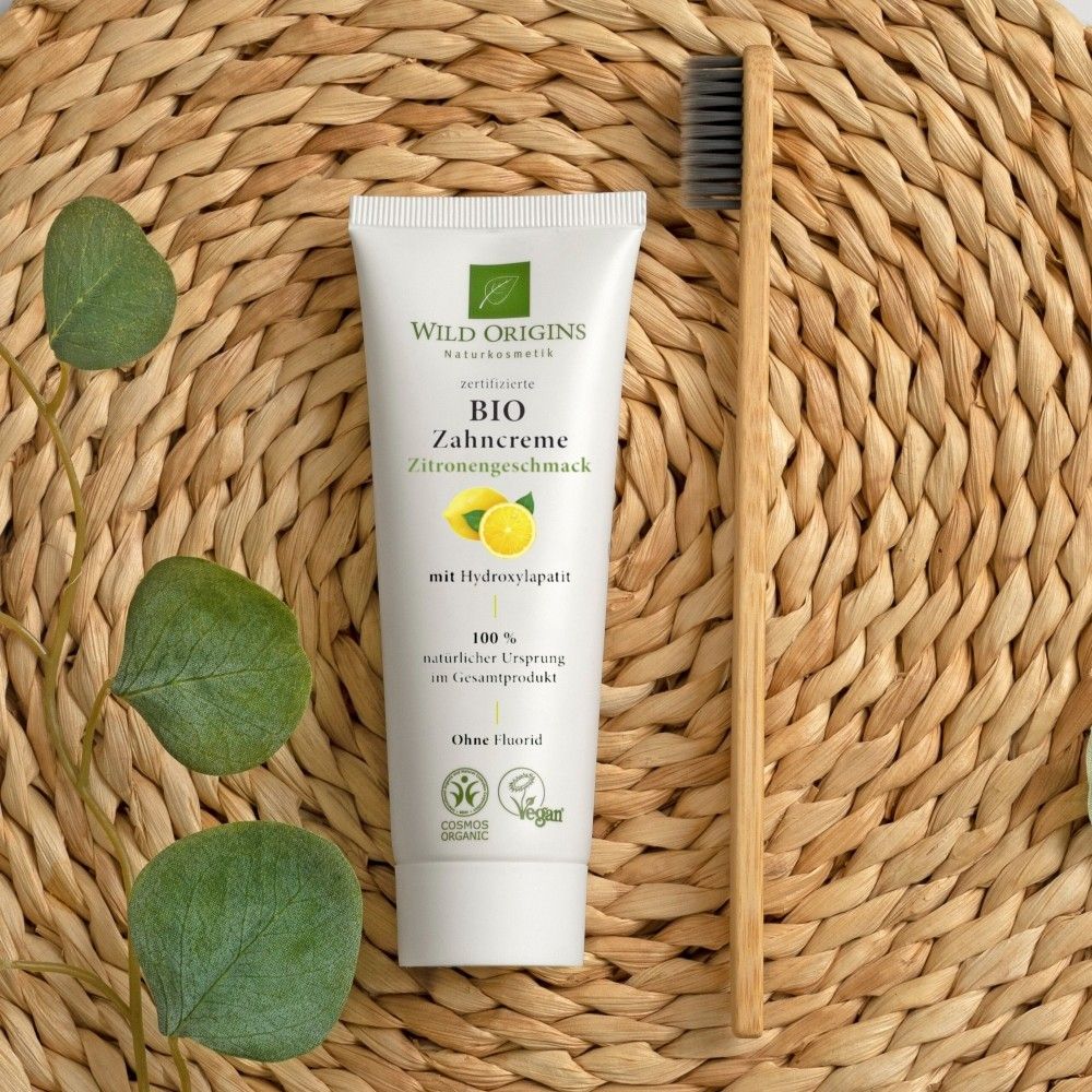 Zahnpasta-Tube neben Holzzahnbürste auf Korbgeflecht. "Wild Origins Bio Zahncreme Zitrone" sichtbar.