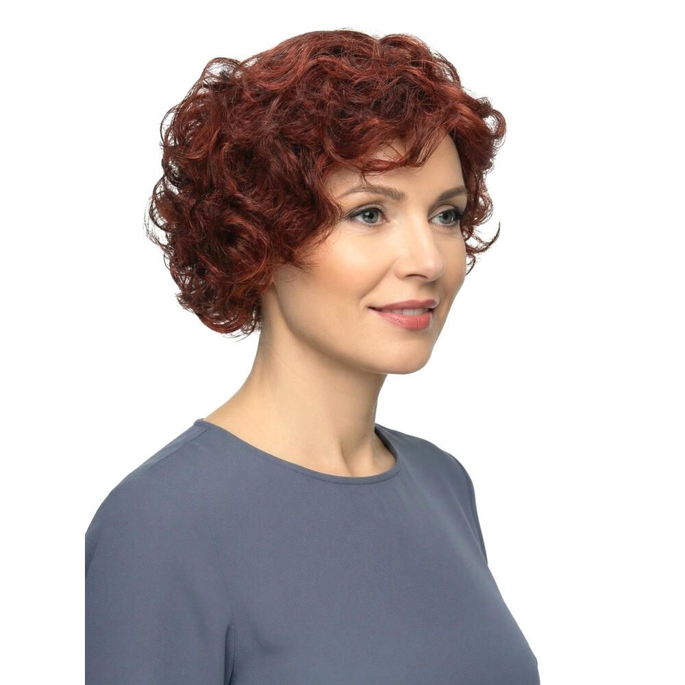 Frau mit roter, lockiger Perücke. Seitenansicht. Kurzes, voluminöses Haar. Bluse in Blau. Weißer Hintergrund.