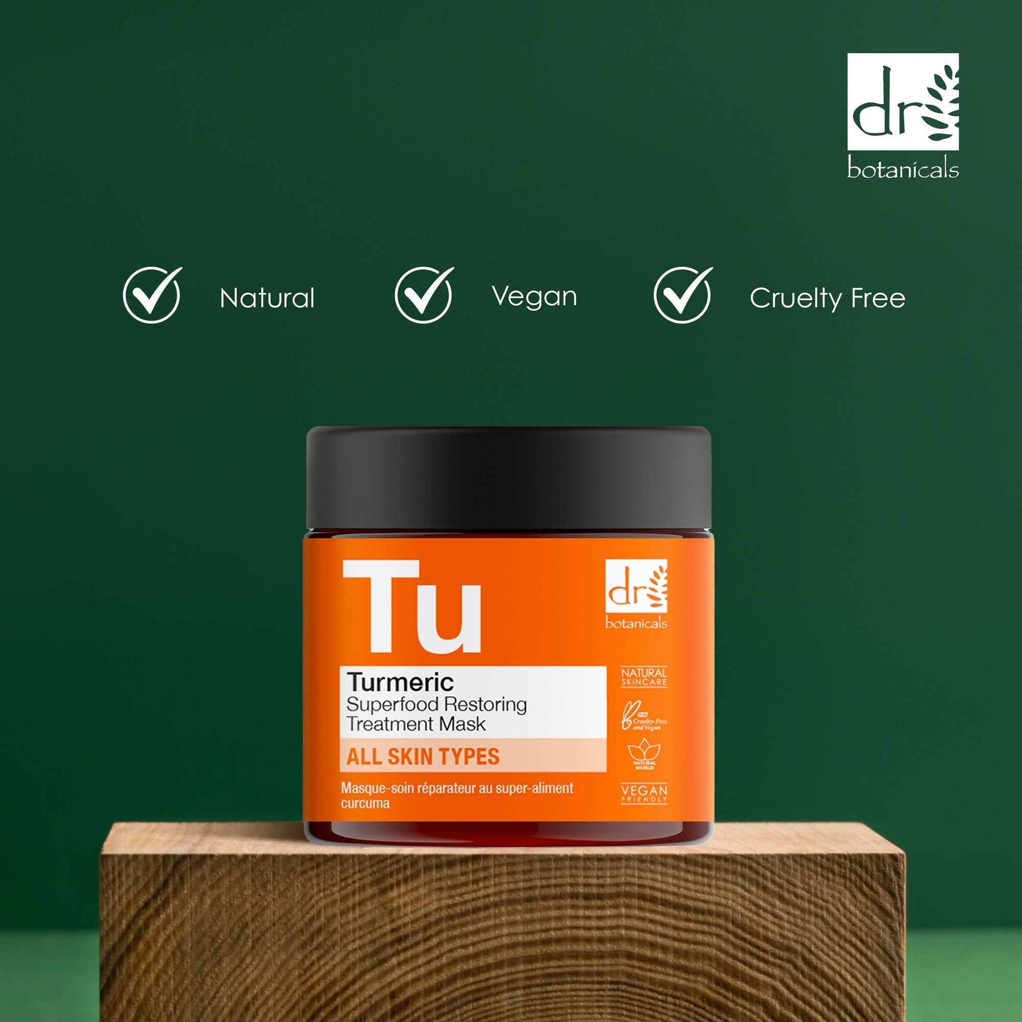 Produkt auf Holzblock. Aufschrift 'Tu' und 'Turmeric Superfood Restoring Treatment Mask'. Orangefarbenes Etikett mit Logo. Symbole: Natural, Vegan, Cruelty Free.