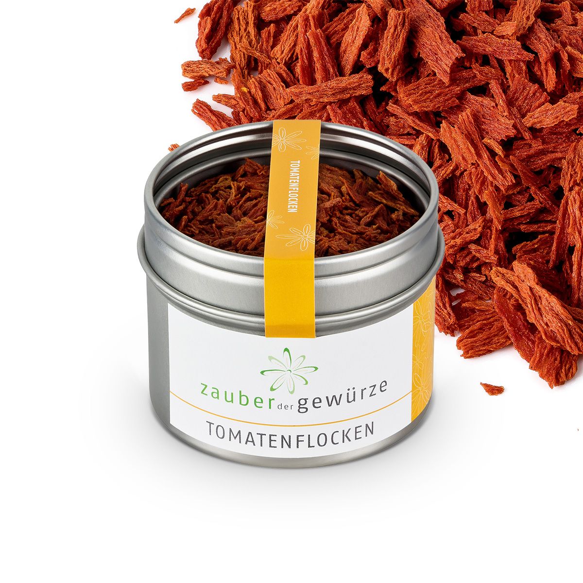 Metallbehälter mit Tomatenflocken, daneben lose Flocken. Gelbes Etikett. Produktname: Zauber der Gewürze Tomatenflocken.