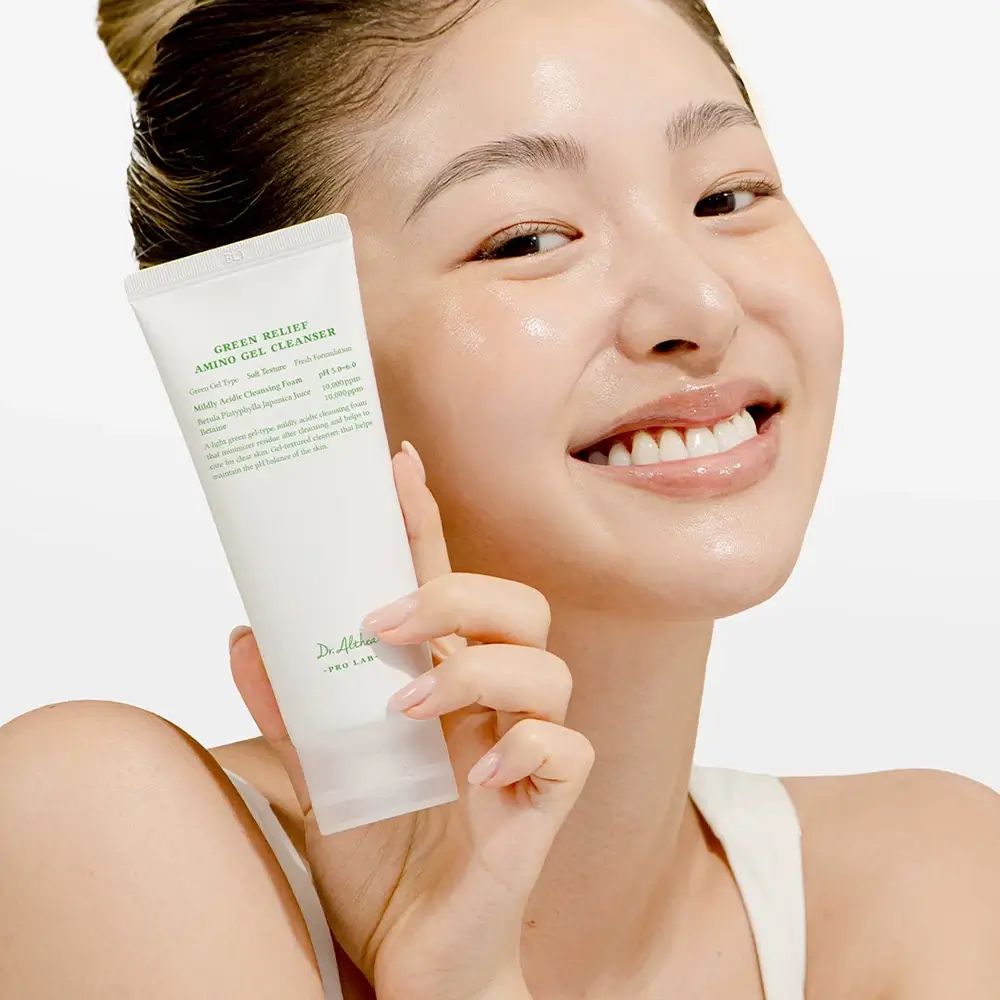 Frau hält eine Tube Green Relief Amino Gel Cleanser. Marke: Dr. Althea. Frau lächelt. Hintergrund: hell.