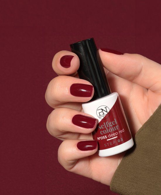 Hand mit lackierten Nägeln in tiefem Rot. Nagellackflasche mit PN-Logo und Beschriftung: selfgel colour, N°055 deep red.