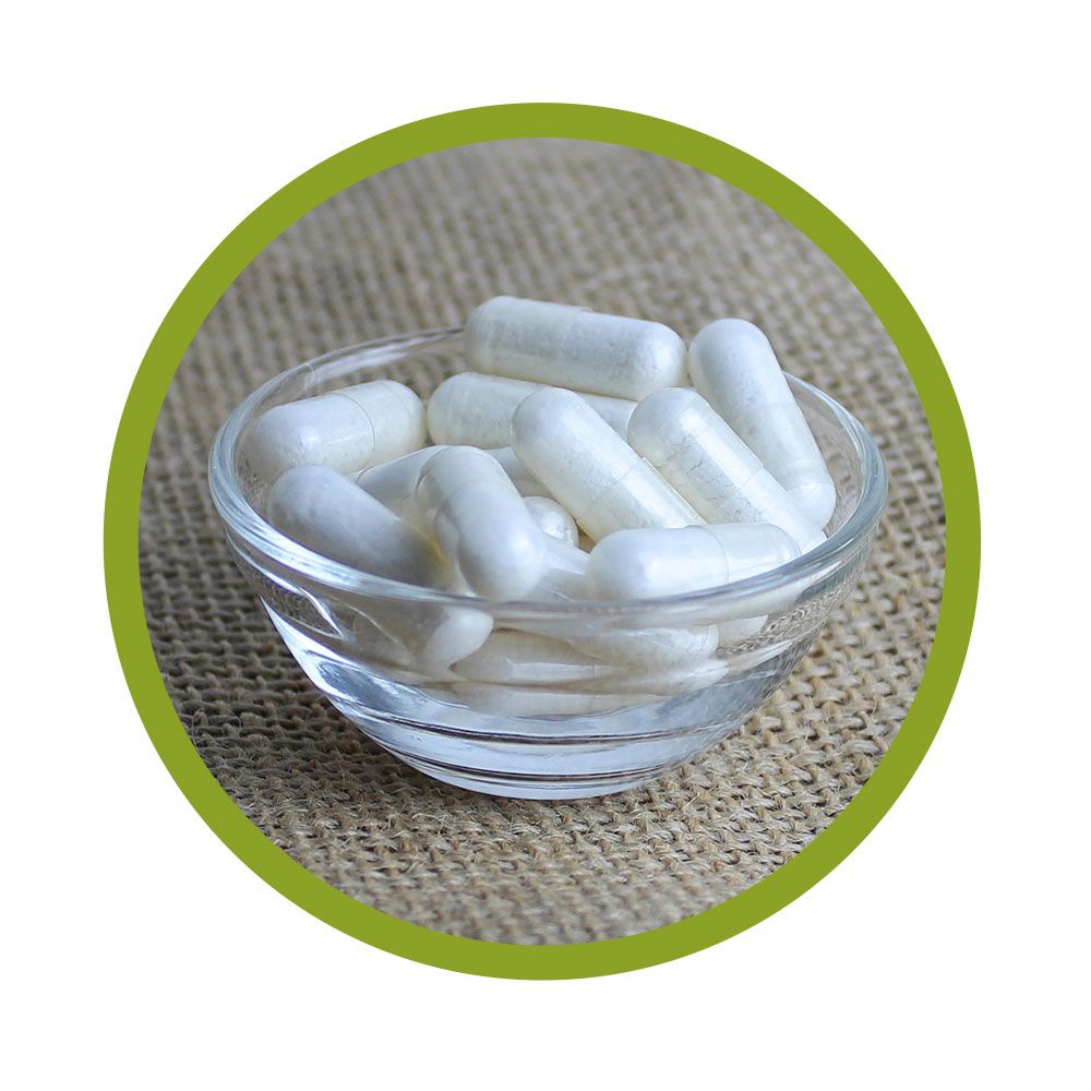 Glasschale mit weißen Kapseln, umrandet von einem grünen Kreis. Auf grobem Untergrund.