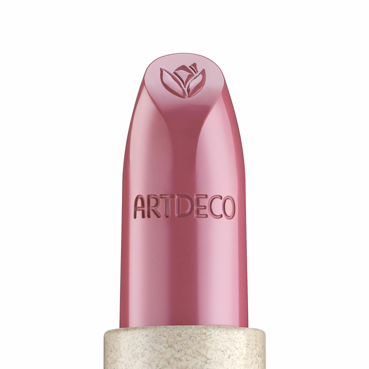 Der Artdeco Natural Cream Lipstick Peony ist in einer hellrosa Hülse mit dem Markennamen eingraviert. Die Lippenstiftspitze trägt ein geprägtes Blütenmotiv. Der Lippenstift selbst hat einen rosafarbenen Farbton. Die Verpackung ist zylindrisch und hat eine glitzernde Textur.