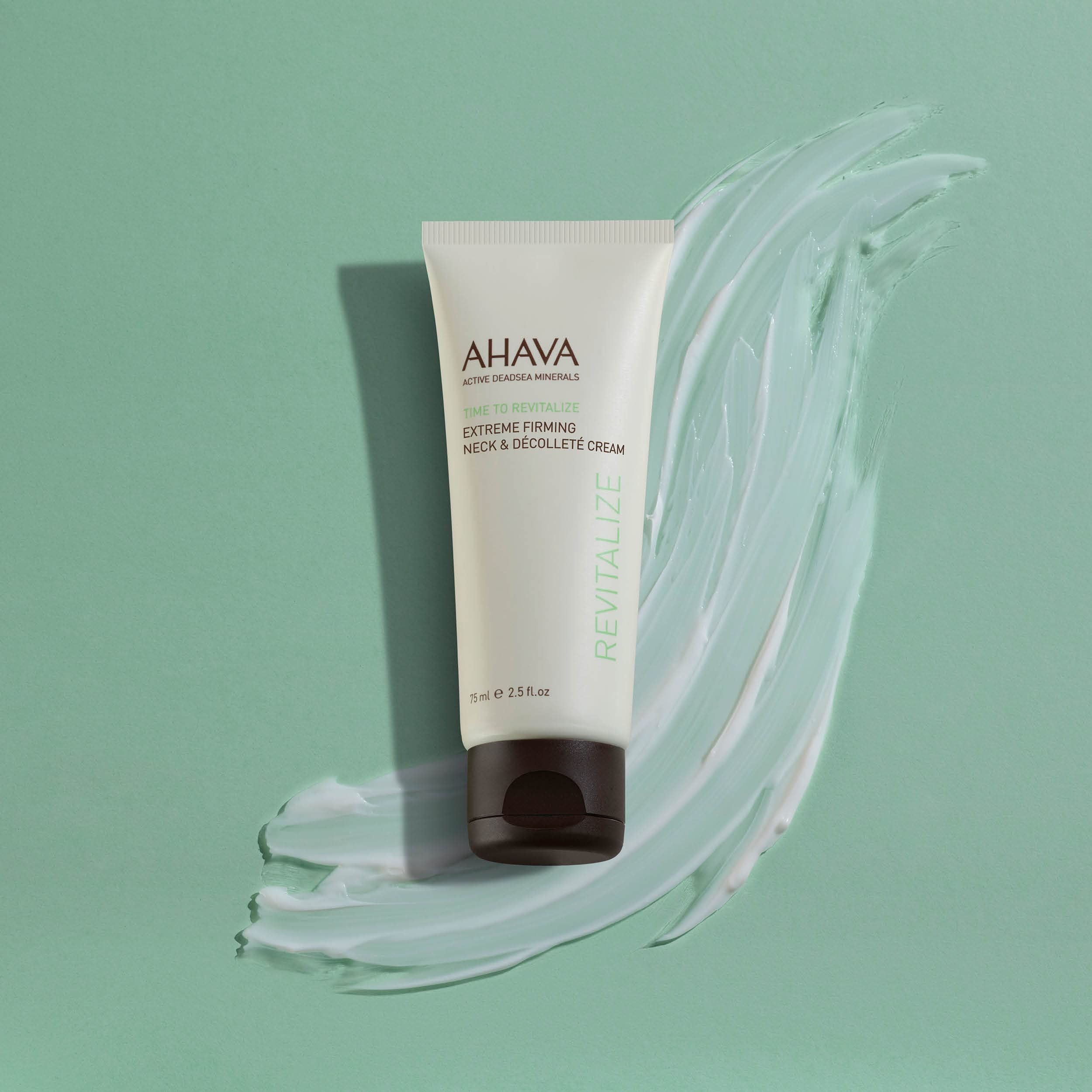 Creme-Tube vor einem Hintergrund mit Creme-Abstrich. Tube mit Produktnamen und -bezeichnung. Text: AHAVA, Time To Revitalize, Extreme Firming Neck & Décolleté Cream.