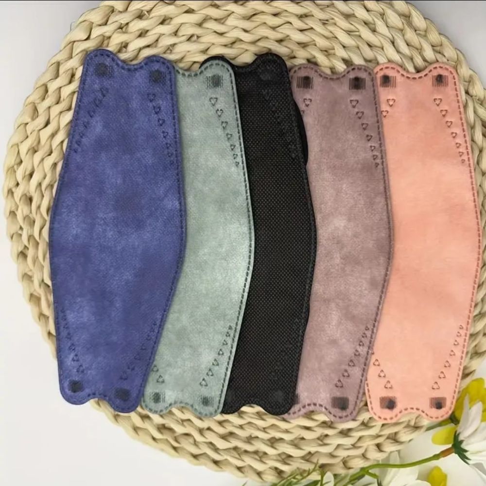 Sechs Gesichtsmasken in verschiedenen Farben: Blau, Grau, Schwarz, Lila und Rosa. Auf einem geflochtenen Untersetzer.