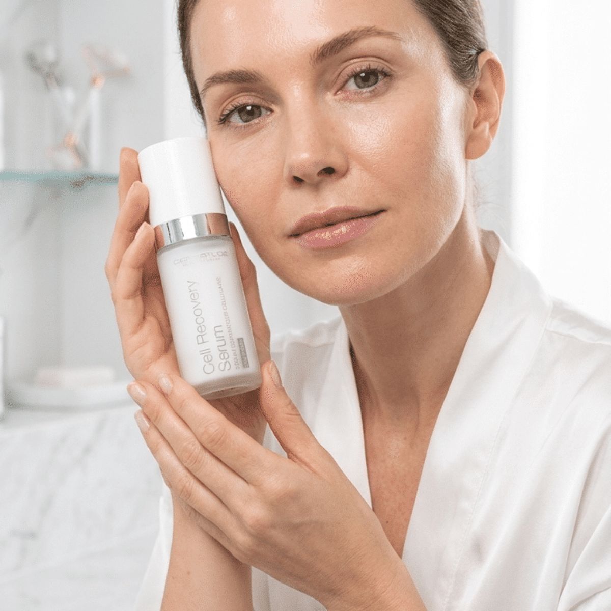 Frau hält Dermatude Cell Recovery Serum Flasche an ihr Gesicht.