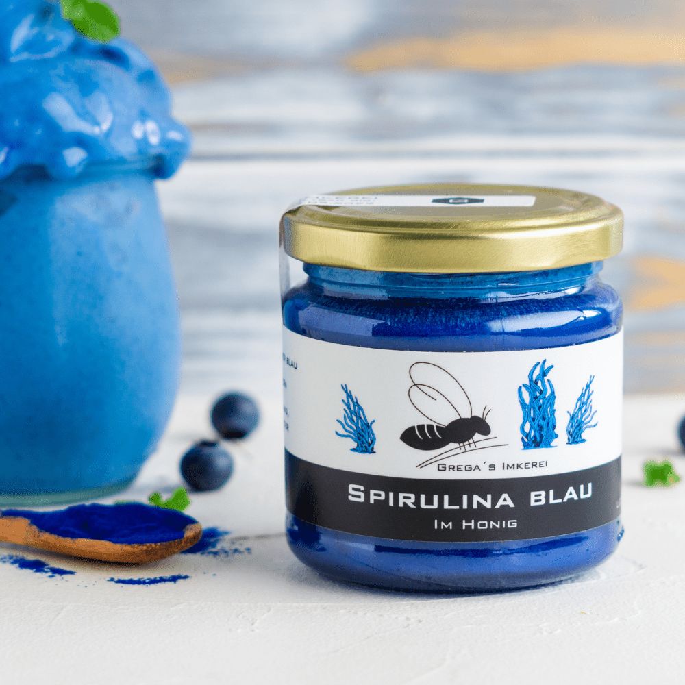 Glas Spirulina Blau Honig neben einem blauen Smoothie und Blaubeeren.