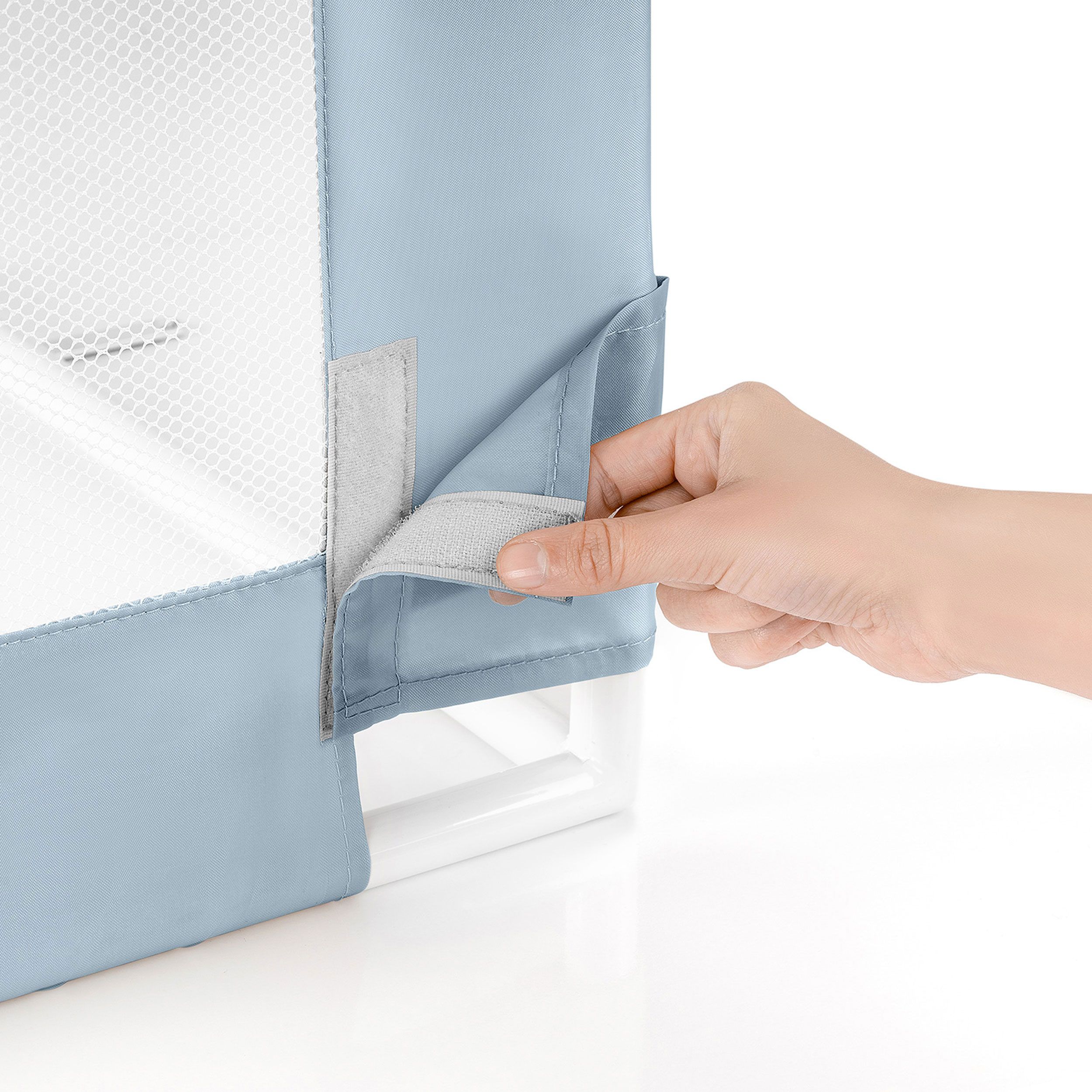 Hand öffnet Klettverschluss am blauen Bettgitter. Weißes Netzgewebe sichtbar.