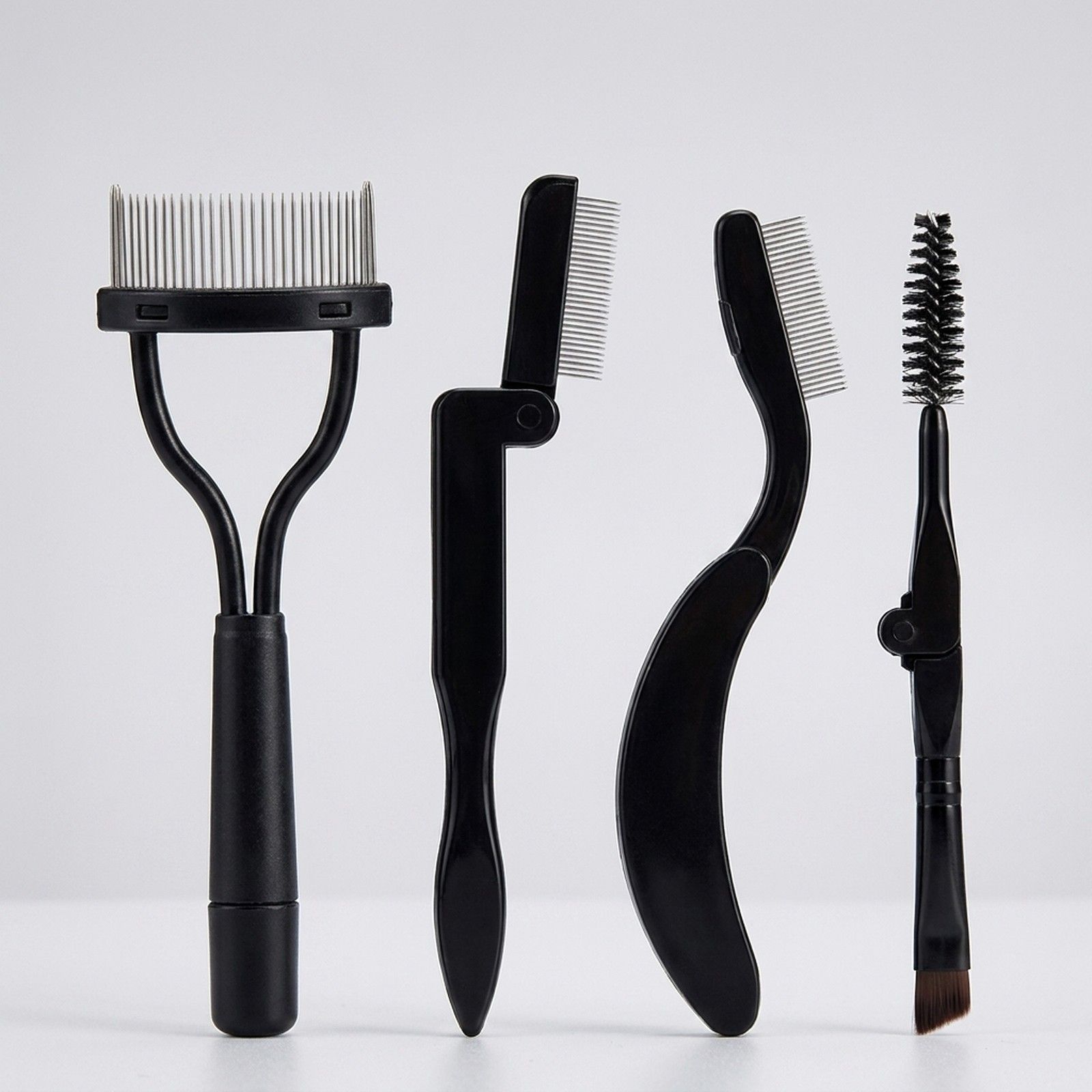 Vier schwarze Werkzeuge für Wimpern und Augenbrauen: Kamm, Klappkamm, gebogener Kamm und Bürste.