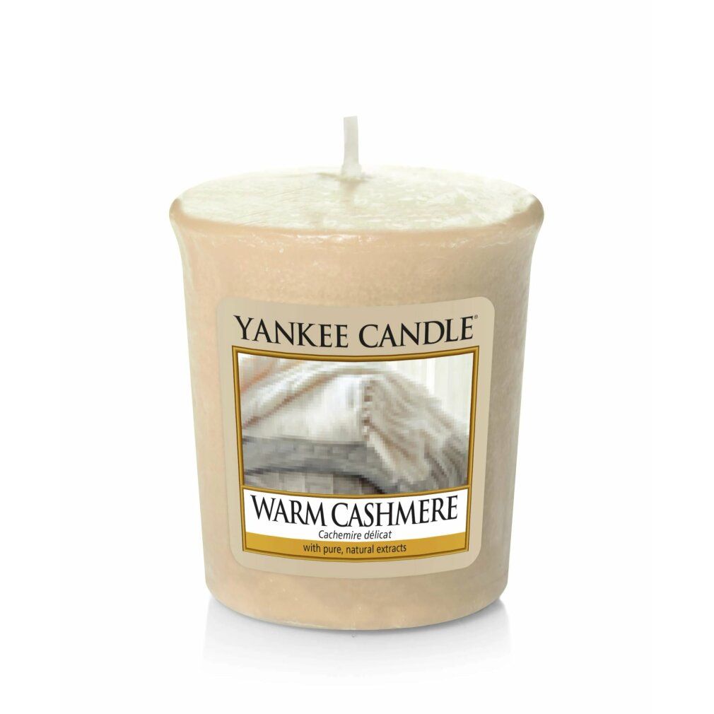 Beige Duftkerze mit Etikett. Aufschrift: Yankee Candle, Warm Cashmere. Abbildung von Decken. Mit Docht.