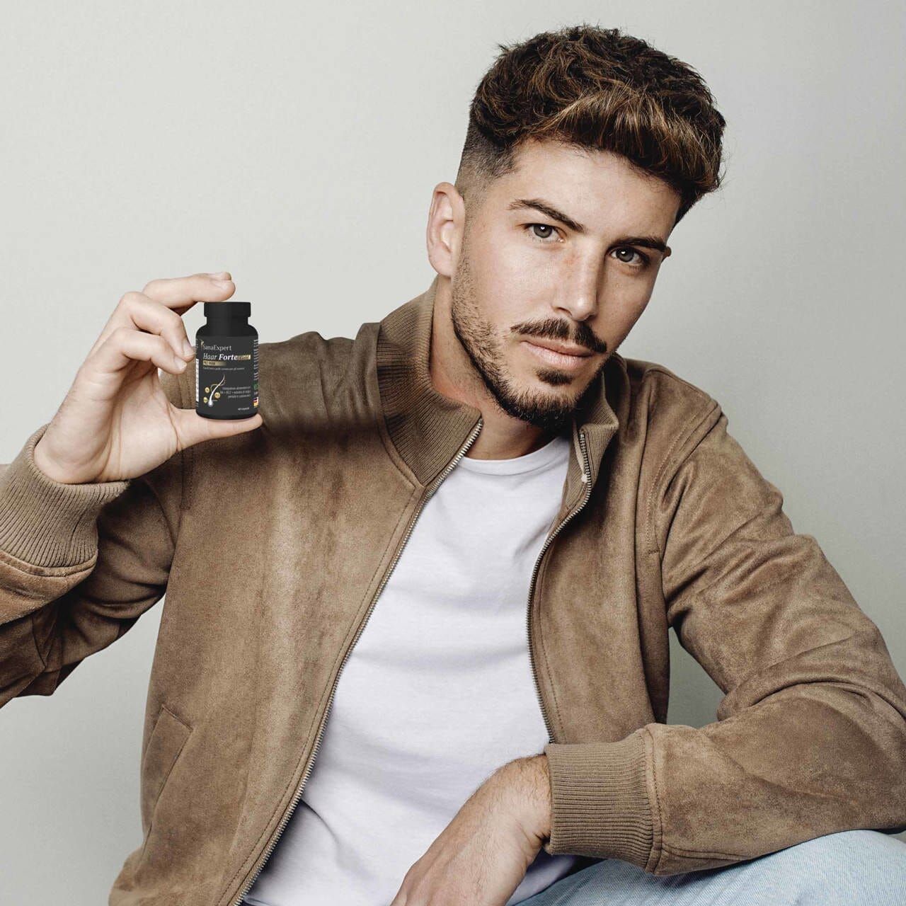Mann hält eine schwarze Flasche SanaExpert Haar Forte Gold Pro Man. Er trägt eine Jacke und schaut in die Kamera.
