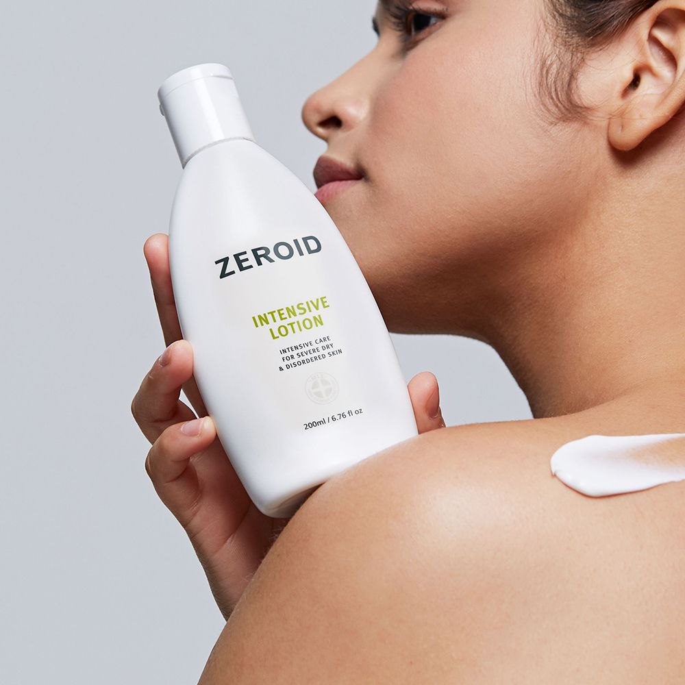 Frau trägt ZEROID Intensive Lotion auf Schulter auf. Weiße Flasche, Text: Intensive Lotion. Creme aufgetragen.