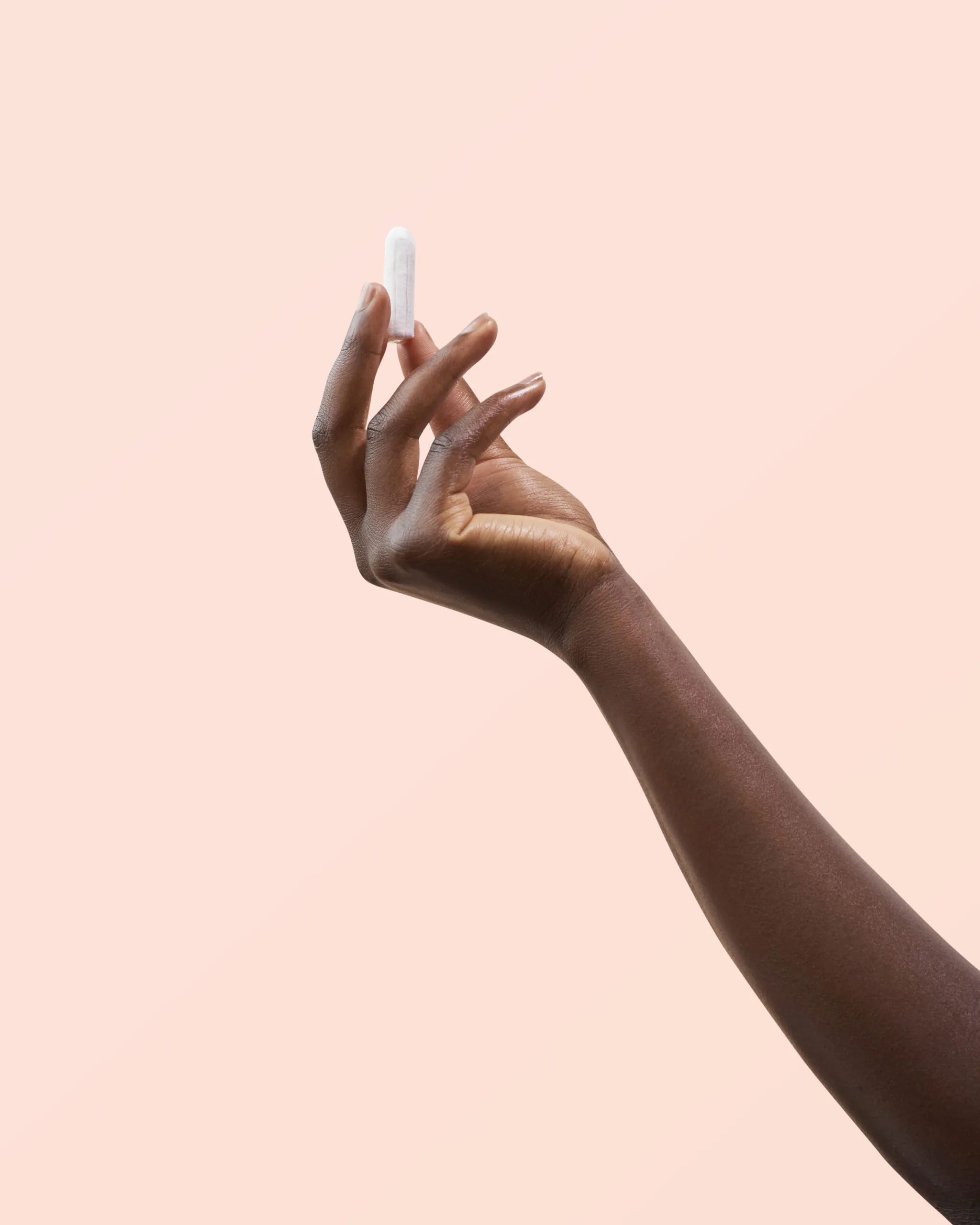 Eine Hand hält einen weißen Tampon. Der Tampon ist zylindrisch.