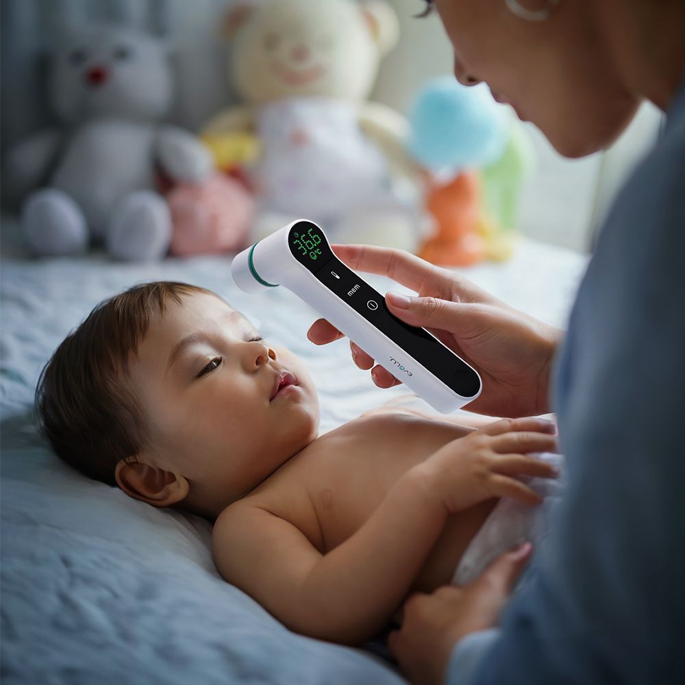 Mutter misst Temperatur bei Baby. Thermometer mit Digitalanzeige. Baby liegt auf dem Bauch.
