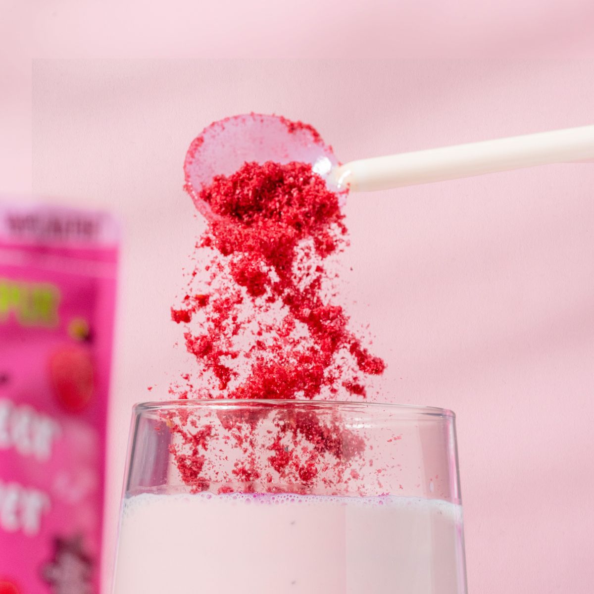 Himbeerpulver wird mit einem Löffel in ein Glas gegeben. Rosa Hintergrund.