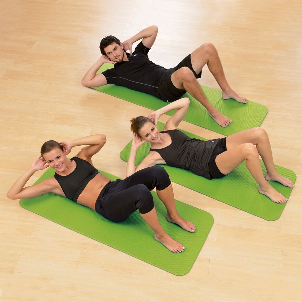 Drei Personen trainieren auf grünen Gymnastikmatten. Die Matten sind rechteckig. Personen machen Sit-ups.