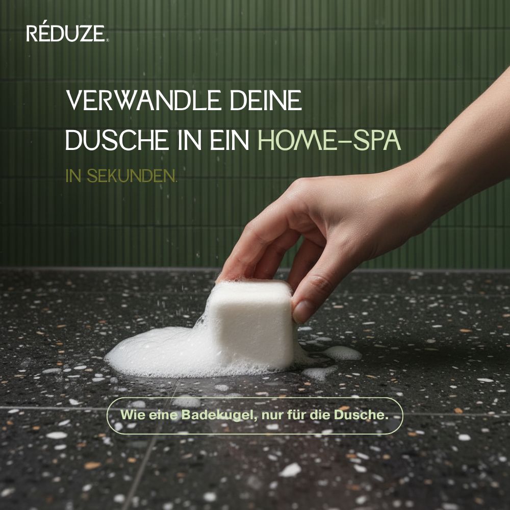 Eine Hand legt einen weißen, quadratischen Duschwürfel auf eine schwarze Oberfläche. Schaum entsteht.