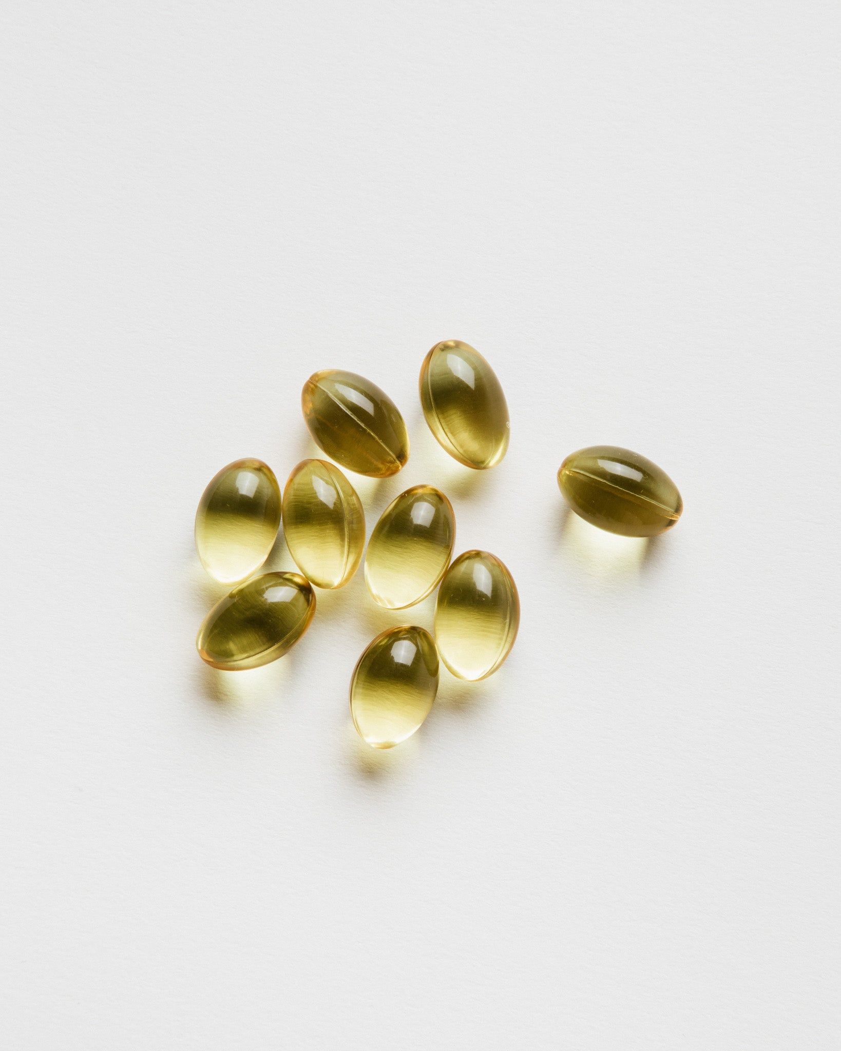 Mehrere gelbliche, ovale Kapseln auf weißem Hintergrund. Einzelne Kapseln sind leicht transparent.
