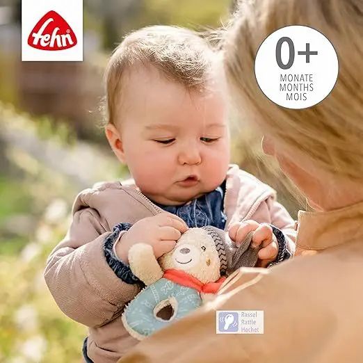 Baby hält Plüsch-Bärchen-Rassel. Fehn-Logo oben links. Altersempfehlung 0+ Monate. Rassel-Icon.