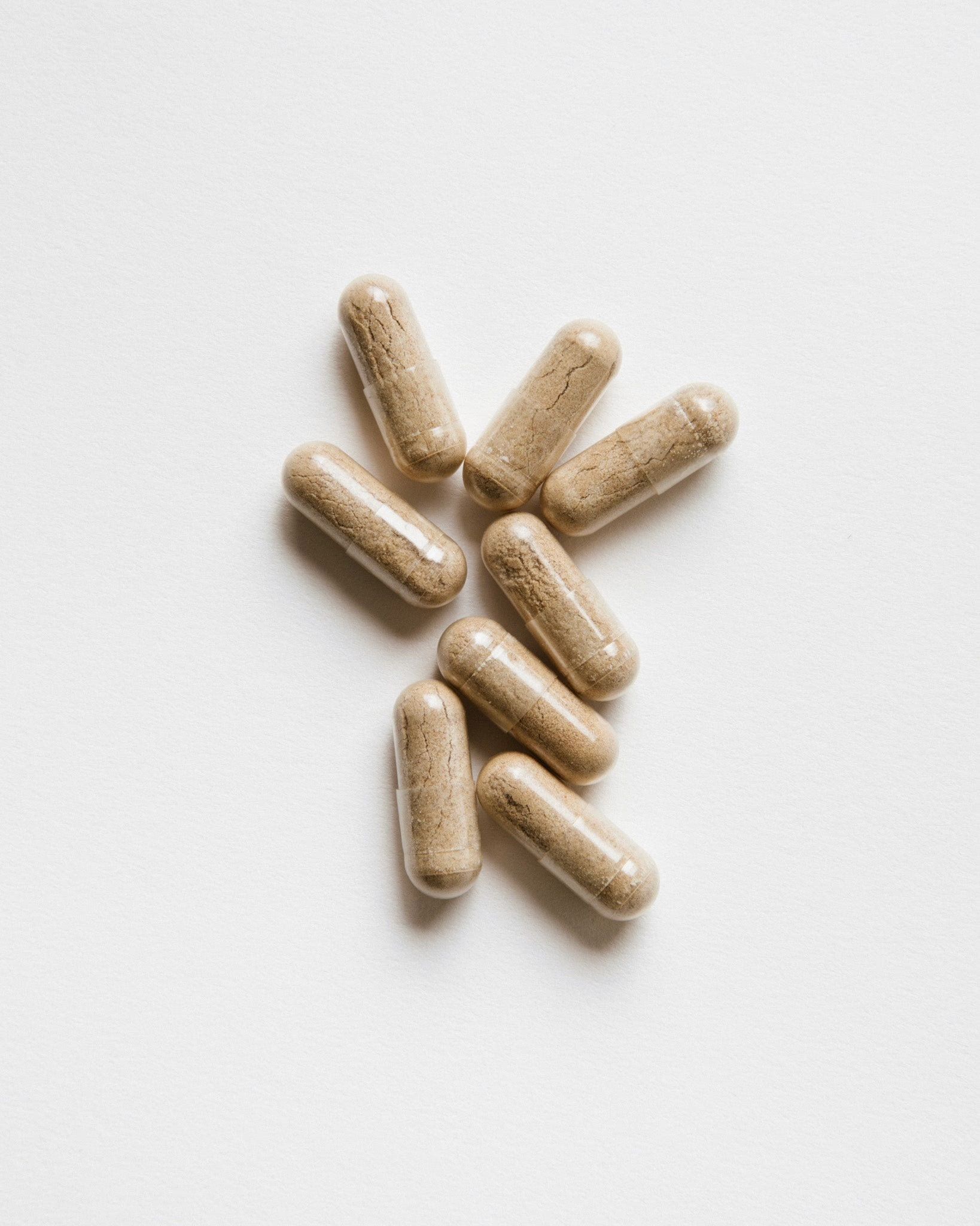 Sieben Kapseln auf weißem Hintergrund. Kapseln sind länglich, hellbraun und liegen verstreut.