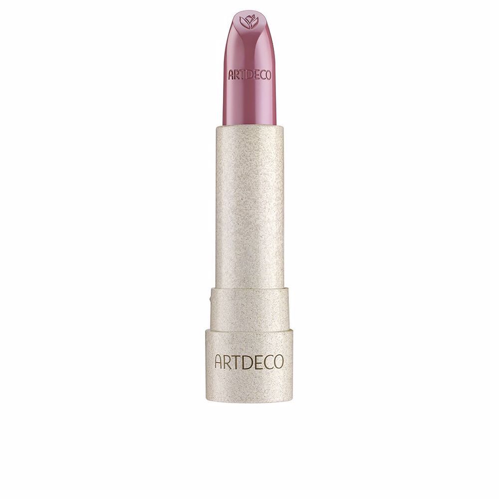 Der Artdeco Natural Cream Lipstick Peony ist in einer hellrosa Hülse mit dem Markennamen eingraviert. Die Lippenstiftspitze trägt ein geprägtes Blütenmotiv. Der Lippenstift selbst hat einen rosafarbenen Farbton. Die Verpackung ist zylindrisch und hat eine glitzernde Textur.