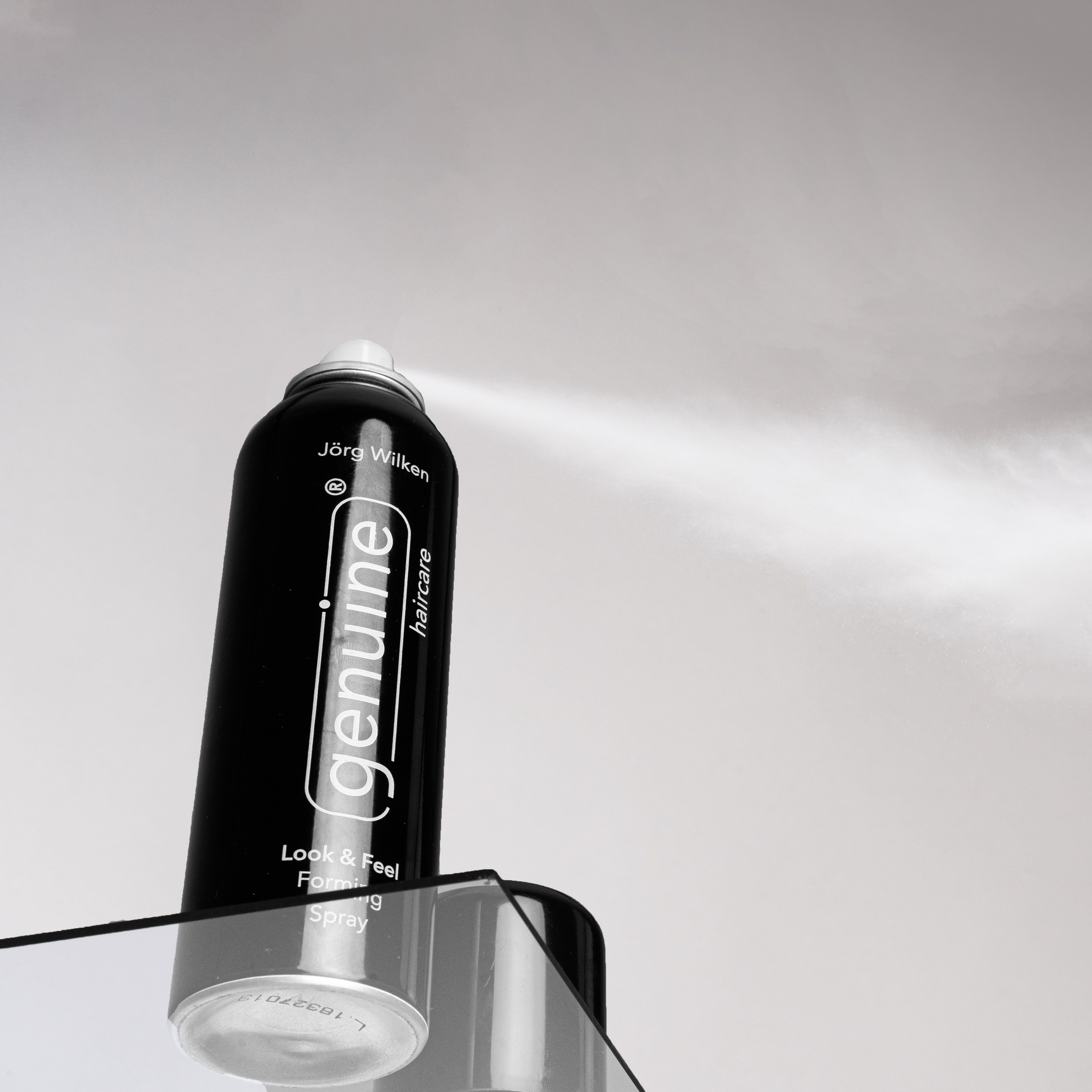 Schwarze Sprühflasche mit weißem Sprühnebel. Aufschrift: genuine haircare, Look & Feel Forming Spray.
