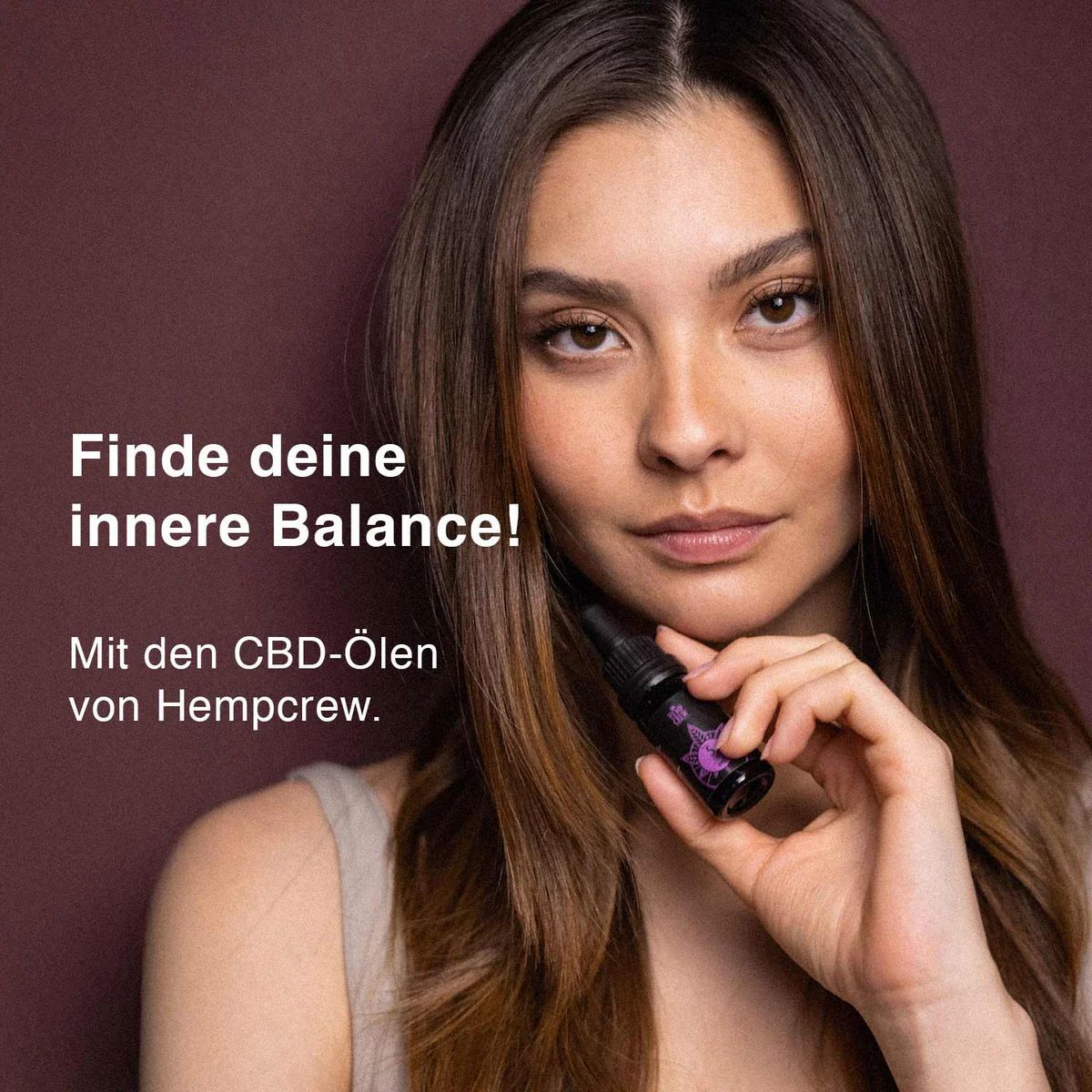 Frau hält eine kleine, schwarze Flasche mit Tropfer. Auf der Flasche ist ein Etikett mit Text und Logo zu sehen.