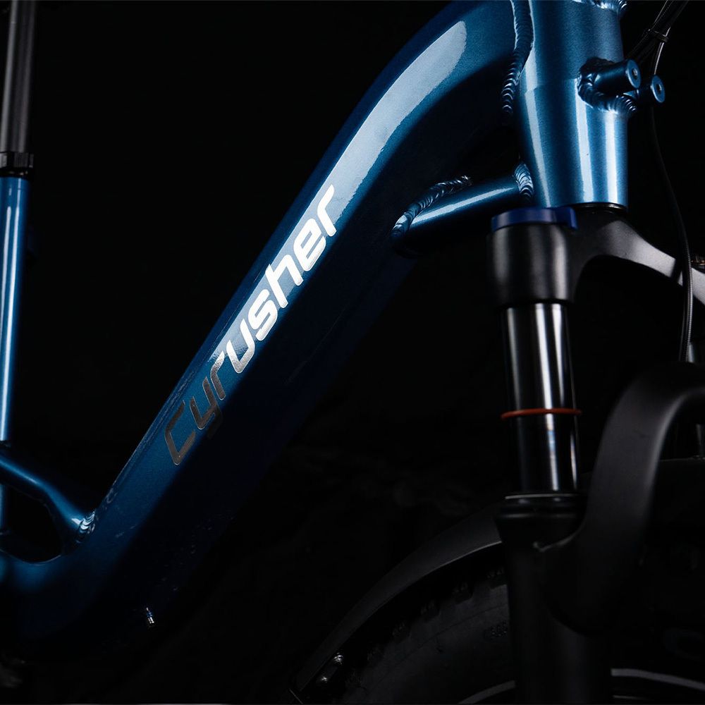 Nahaufnahme des Rahmens eines blauen E-Bikes. CYRUSHER-Logo in Weiß. Vorderradaufhängung.