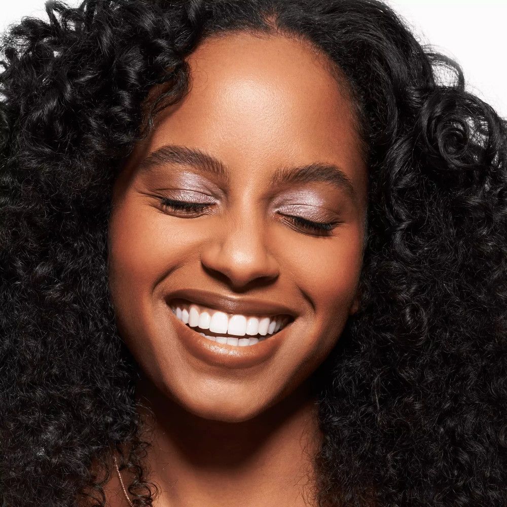 Porträt einer lächelnden Frau mit braunem Lippenstift. Lockiges Haar, geschminkte Augen.