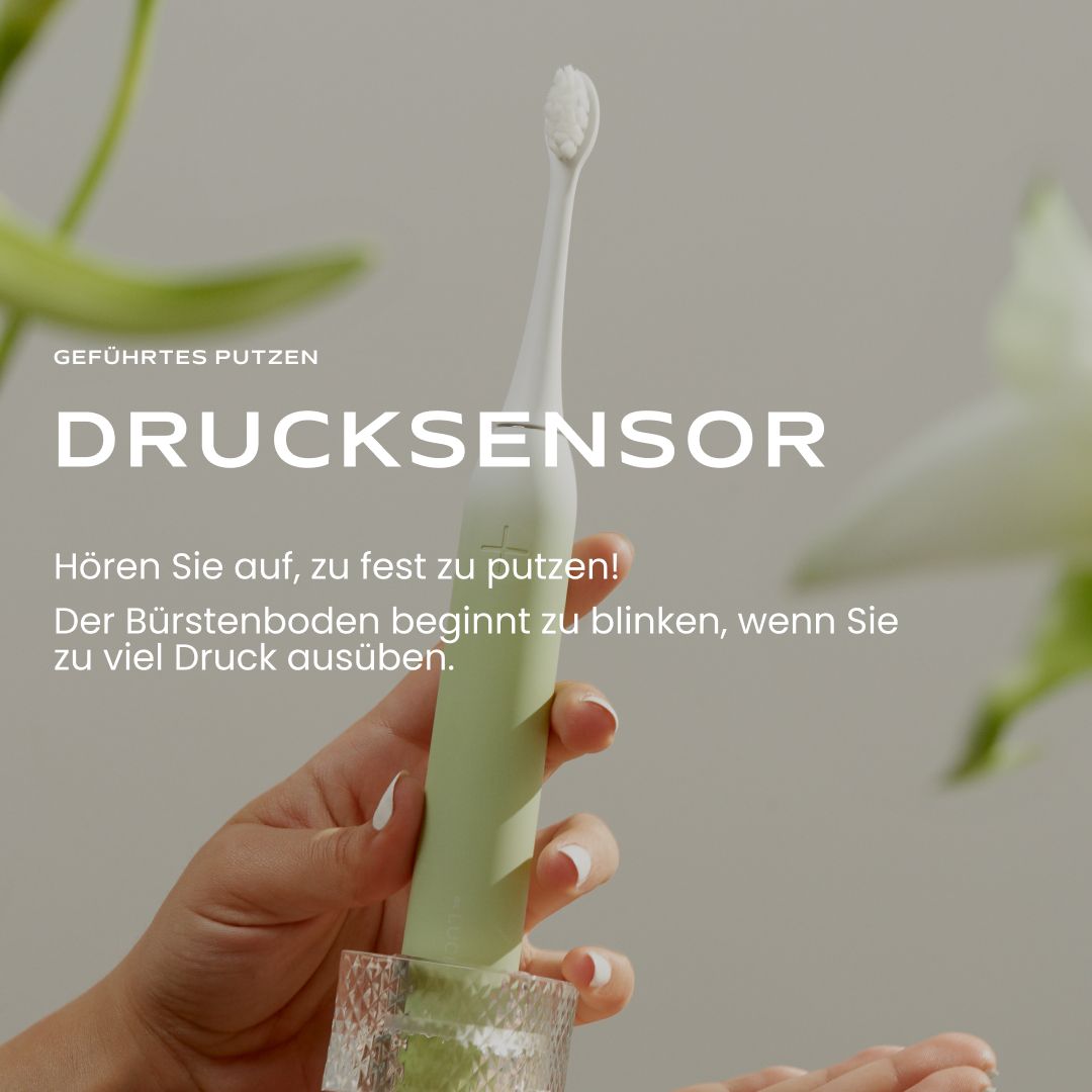 Hand hält eine grüne Be Lucent Prism Sonic Elektrische Zahnbürste mit Drucksensor.