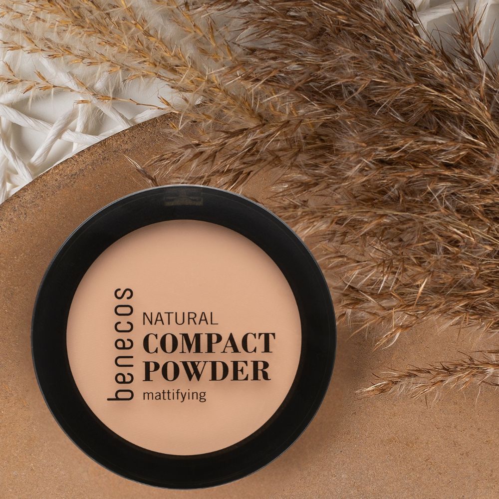 Benecos Natural Compact Powder mattifying, Porzellan. Schwarzer Behälter mit hellem Puder, neben Gräsern.